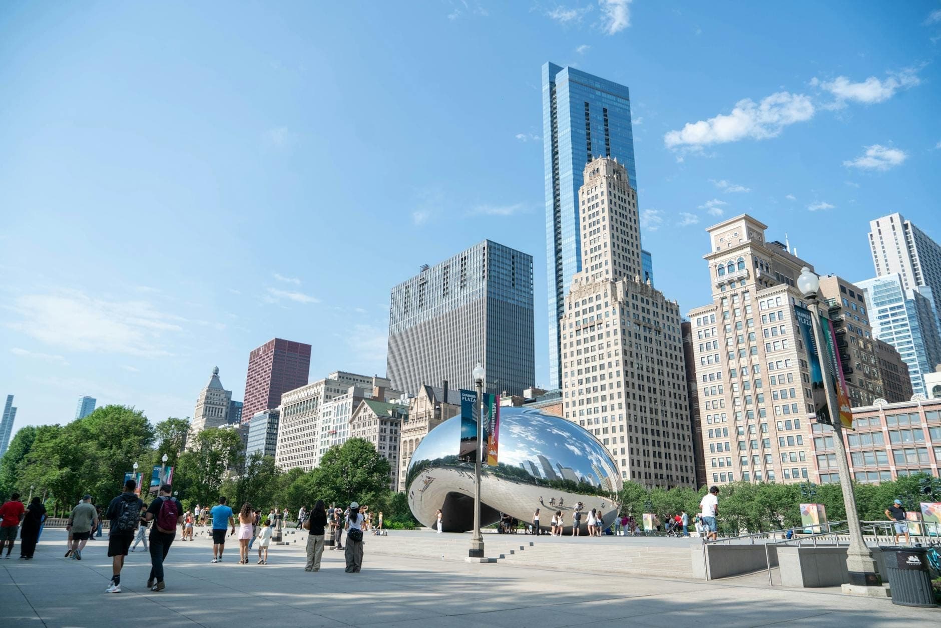People walking around Millennium Park with The Bean sculpture and Chicago skyline in the background on a sunny day.