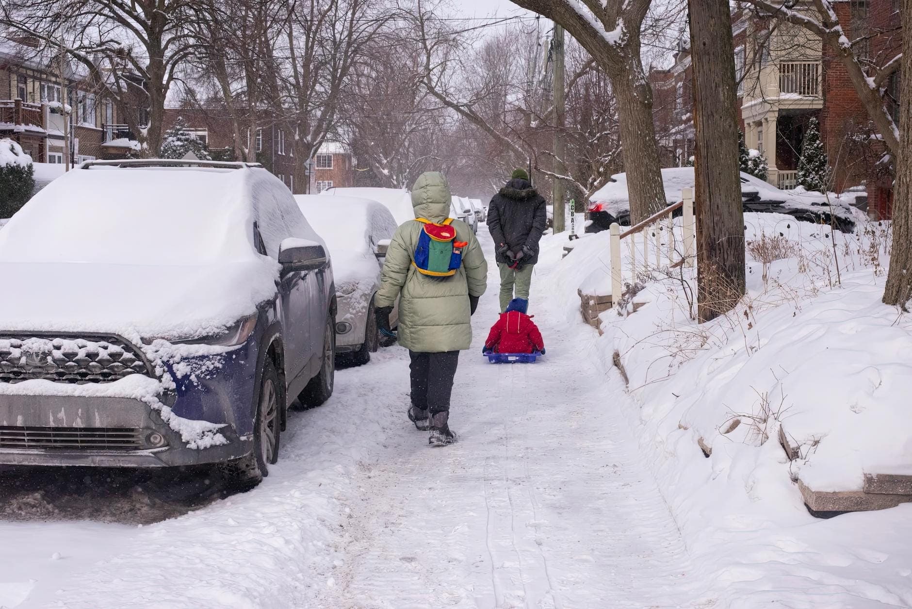 Kinder und Erwachsene gehen und ziehen einen Schlitten durch eine schneebedeckte Wohnstraße in Chicago nach einem Wintersturm.