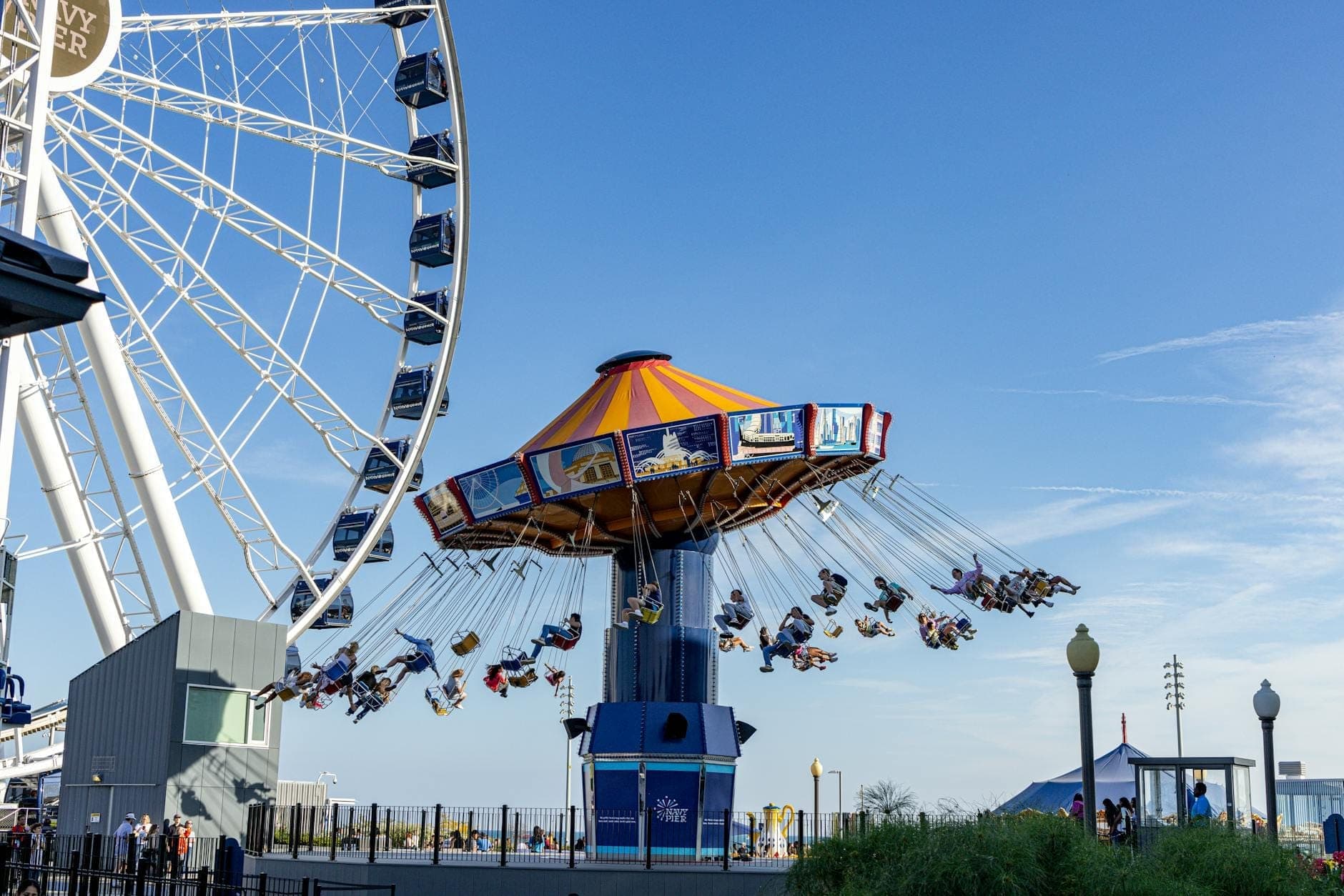 Children and families riding a colorful swing ride near a large Ferris wheel at Chicago’s Navy Pier on a sunny day.