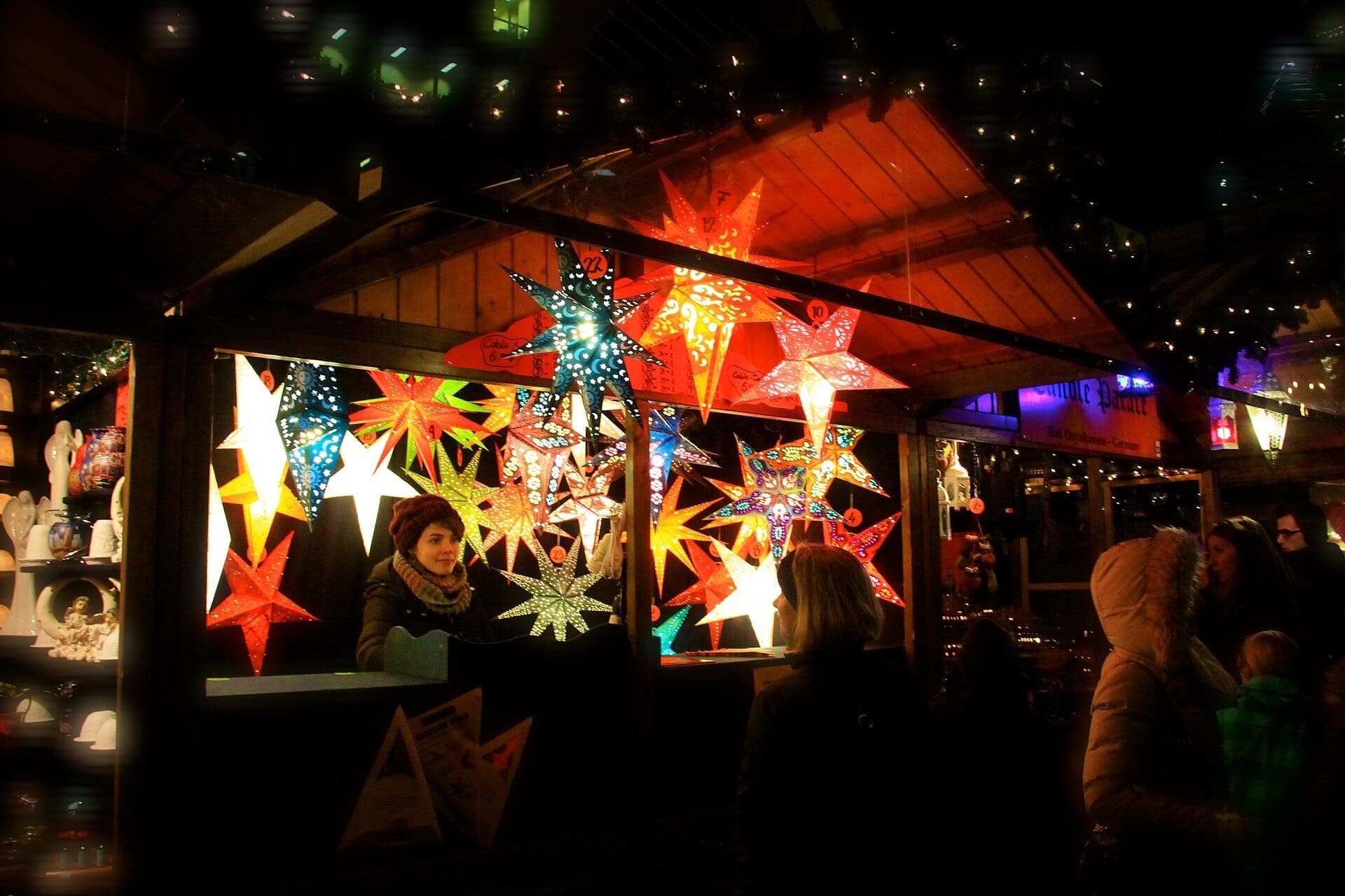 A brightly lit Christkindlmarket Chicago stall at night, decorated with colorful star lanterns and attended by bundled-up visitors in winter clothing.
