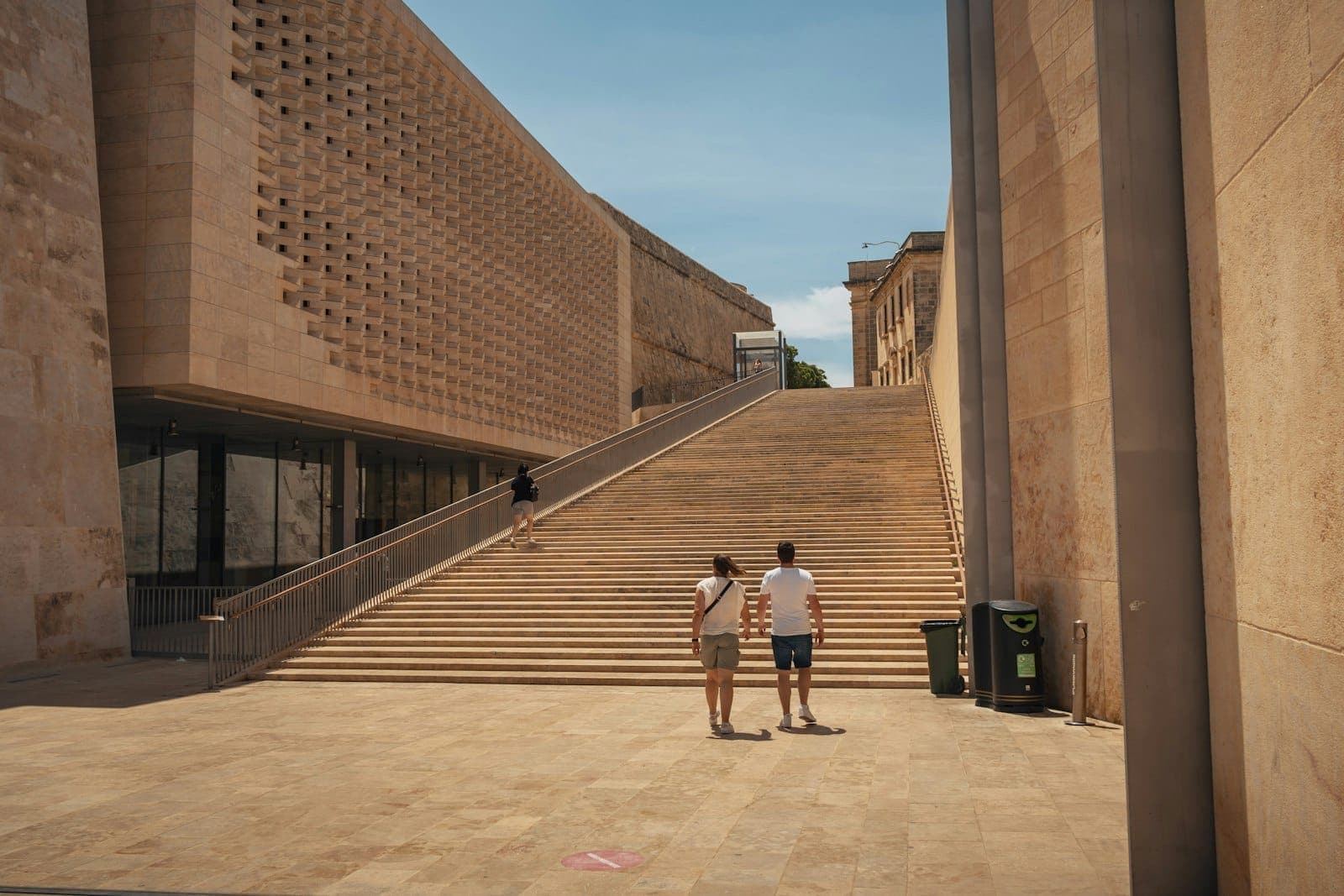Breite Steinstufen, eingerahmt vom Parlament und dem Valletta City Gate von Renzo Piano, mit modernen Kalksteinfassaden unter klarem Himmel.