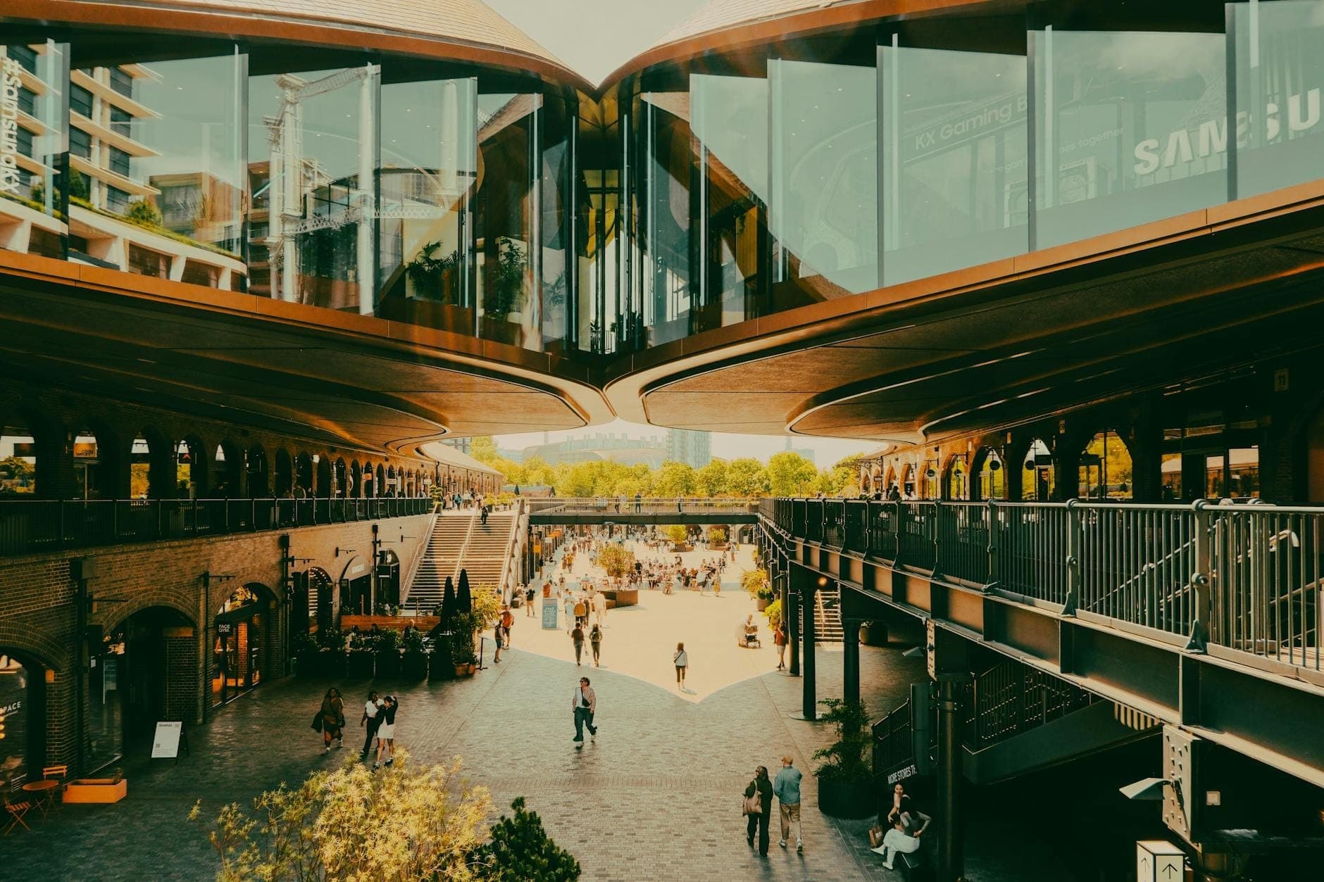 Wide view of Coal Drops Yard’s central courtyard with restored Victorian architecture, elevated walkways, shops, and people relaxing in a lively outdoor setting.