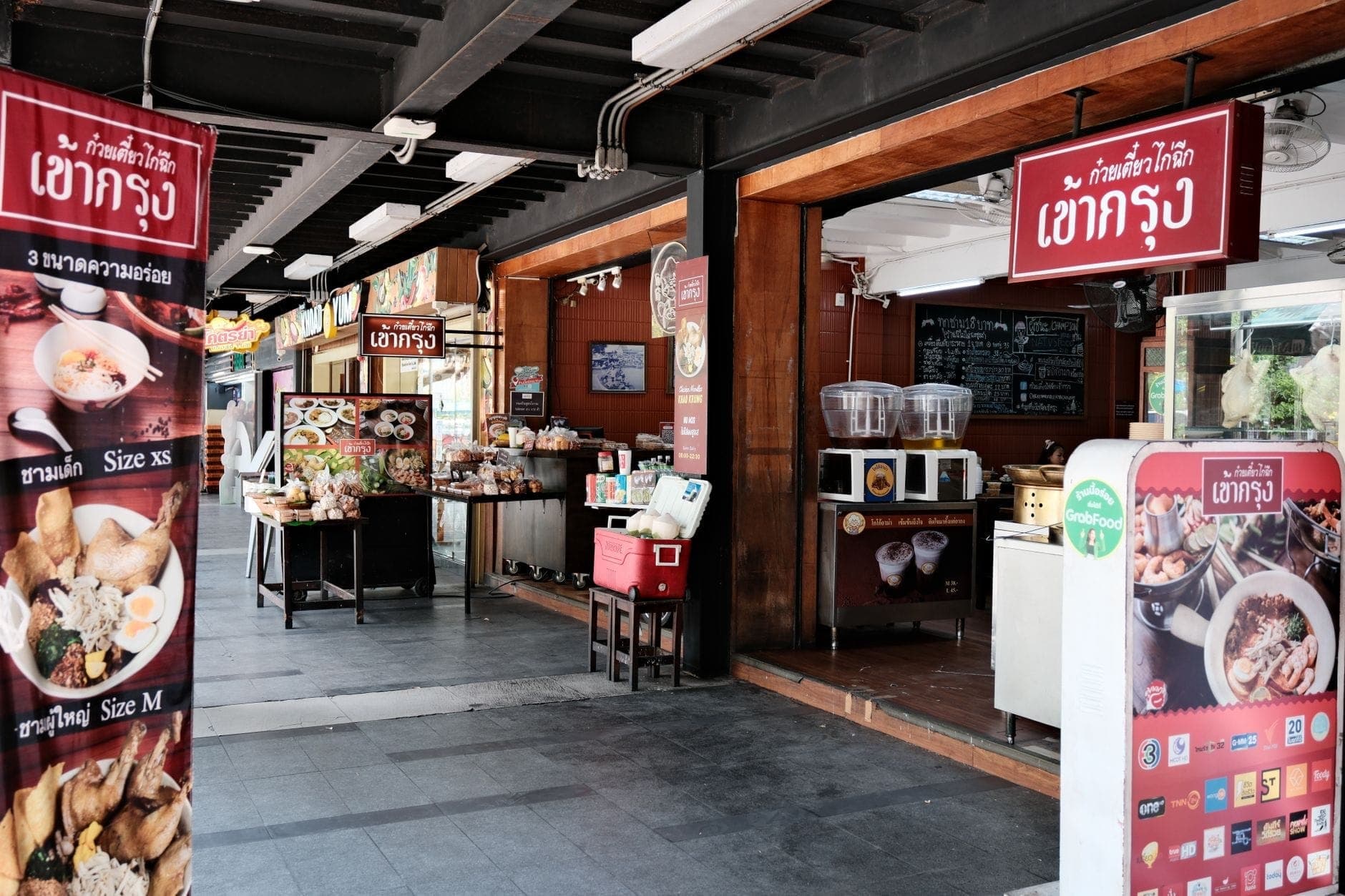 Ristorante tailandese luminoso e aperto sul fronte con insegne colorate ed esposizione di cibo, tipico della vivace scena culinaria di Chiang Mai.