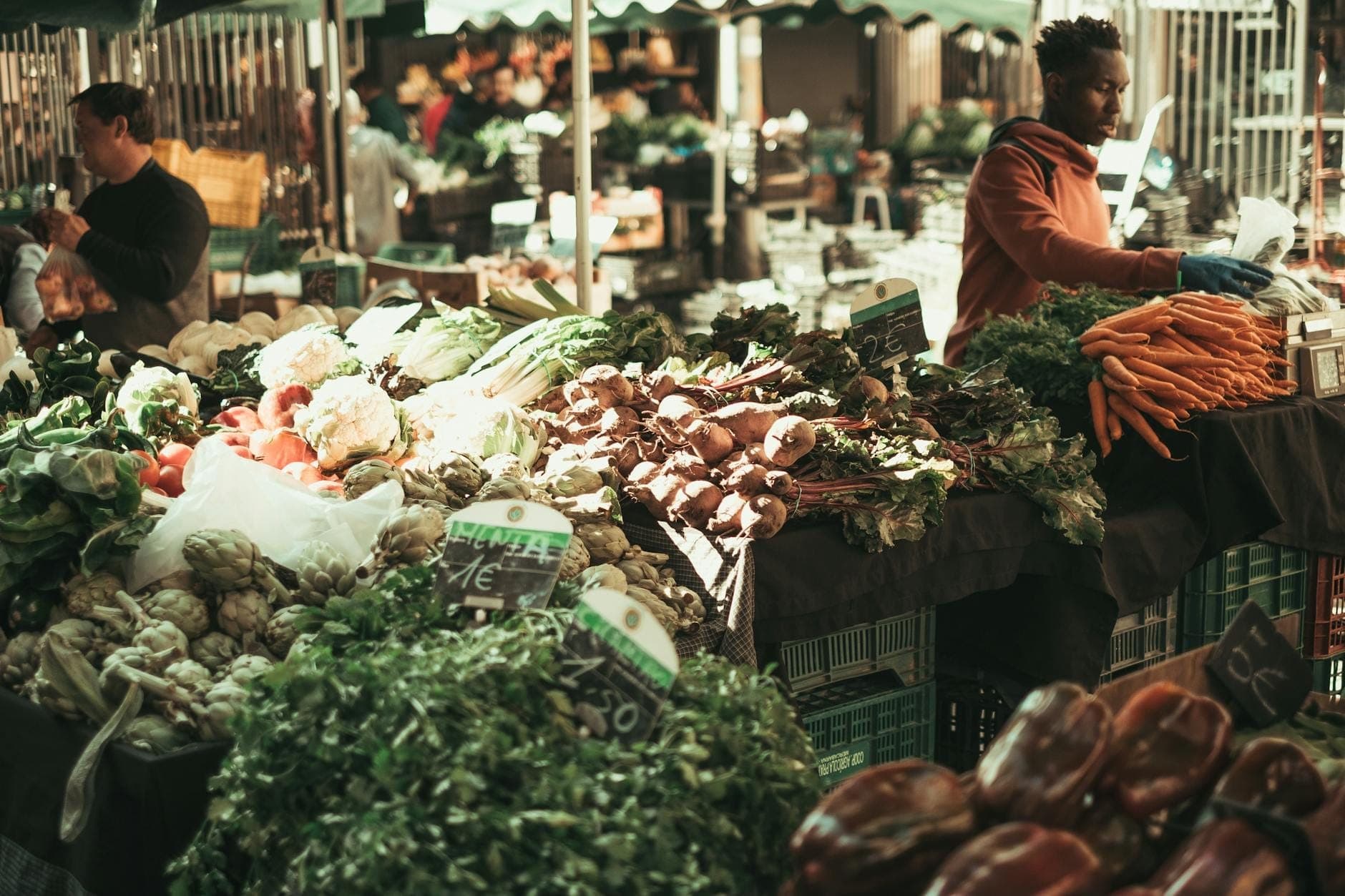 Belebter Freiluftmarkt auf Kreta mit Händlern, die frisches saisonales Gemüse wie Artischocken, Karotten, Blattgemüse und Kräuter anbieten.