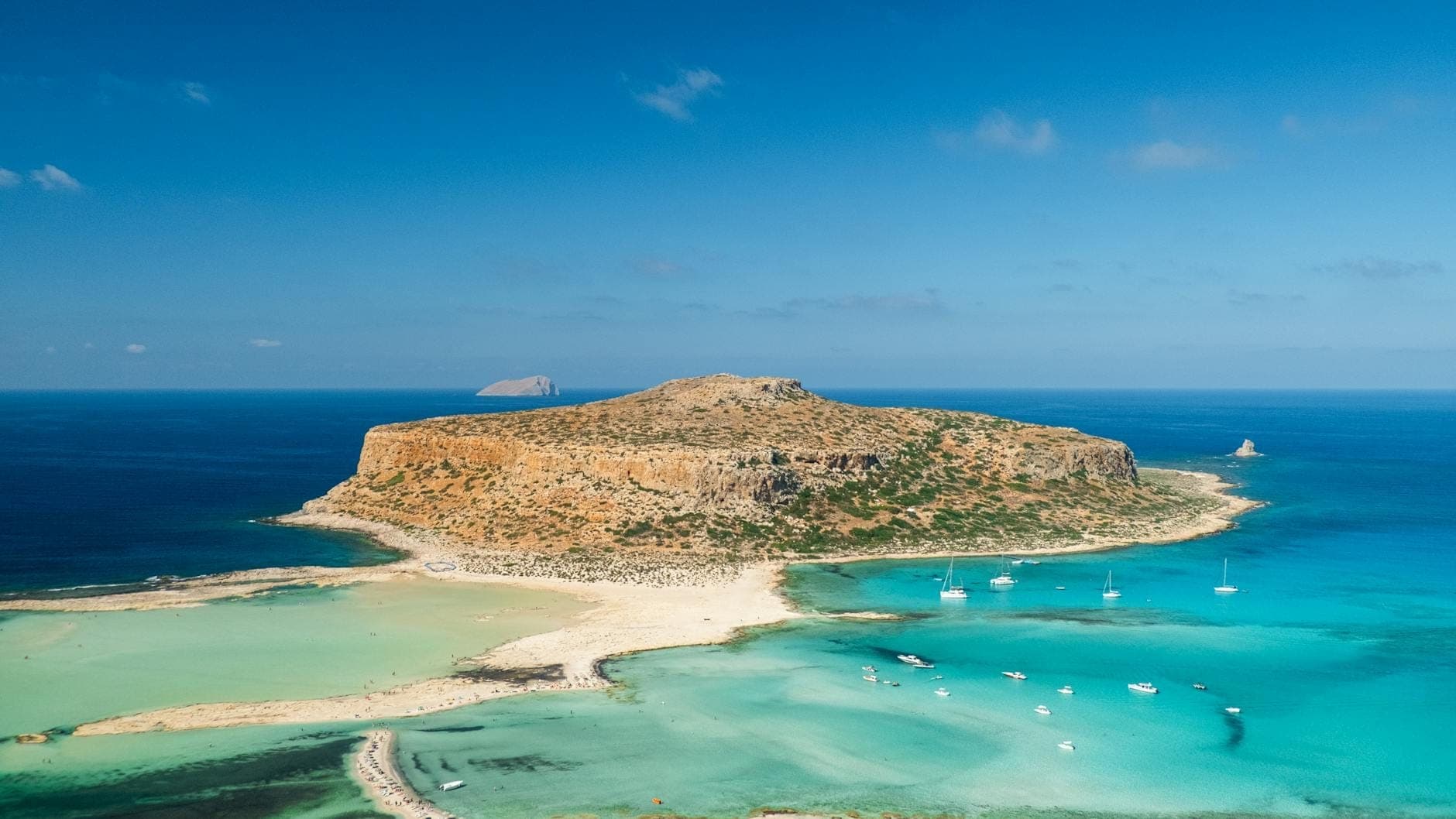Atemberaubender Blick auf die türkisfarbene Balos-Lagune mit ihrem sandigen Isthmus und mehreren Booten im kristallklaren Wasser, Kreta, Griechenland.
