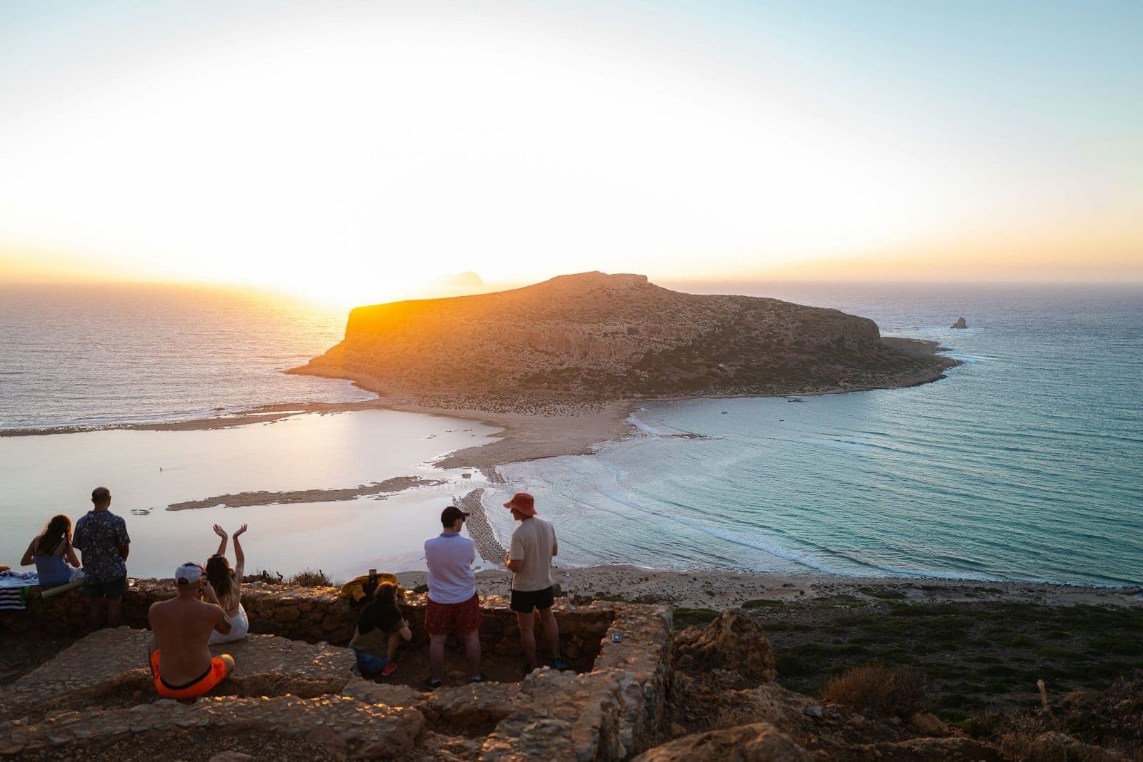 Paar beobachtet einen atemberaubenden Sonnenuntergang über der Balos-Lagune auf Kreta – Meer, Klippen und Insel in goldenes Licht getaucht, eine zutiefst romantische Atmosphäre.