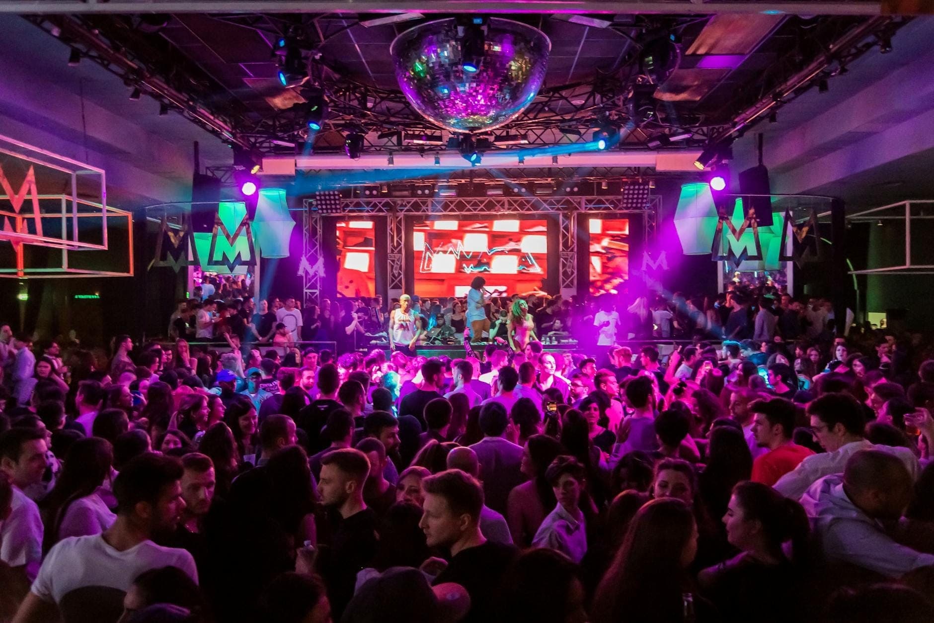 Lebhafte Clubszene mit einer großen tanzenden Menge unter bunten Lichtern und einer Diskokugel – ausgelassene Partystimmung auf Kreta.