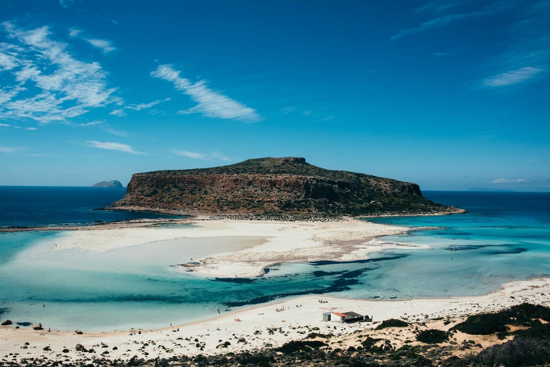 Ein atemberaubendes Panorama einer sonnenbeschienenen Lagune mit türkisfarbenem Wasser und einer felsigen Insel, eingerahmt von blauem Himmel und Sandstränden in Griechenland.