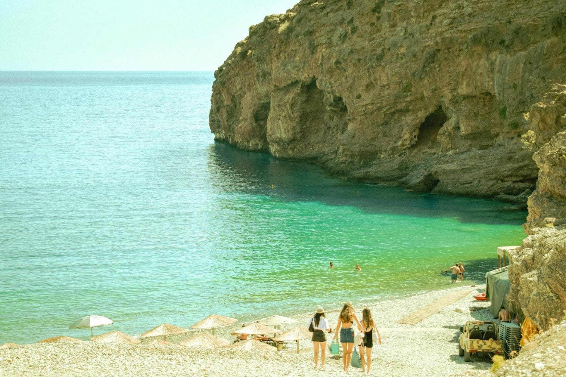 Drei Kinder und ein Erwachsener laufen zu einer malerischen, geschützten Bucht mit türkisblauem Wasser und Felsklippen auf Kreta – ein perfekter Ausflug für Familien.