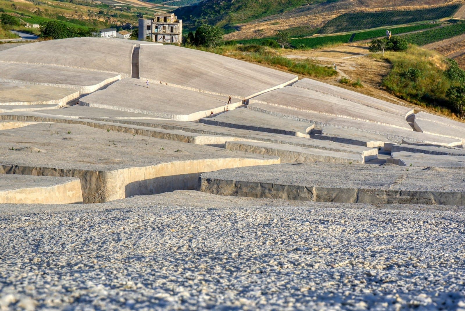 Pemandangan luas blok beton putih Cretto di Burri dengan pengunjung yang tersebar dan sebuah bangunan terbengkalai, di pedesaan Sisilia.