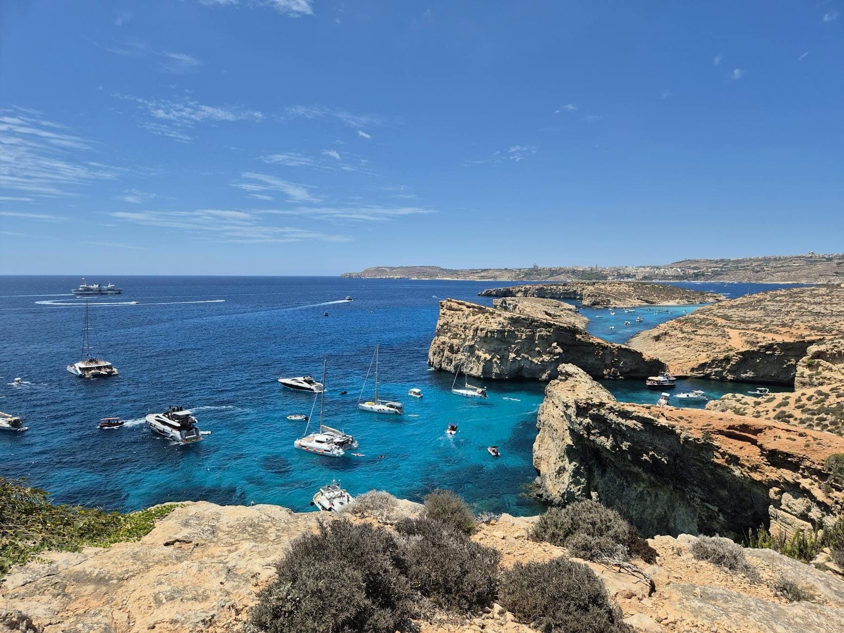 Beeindruckender Blick auf die Crystal Lagoon mit türkisfarbenem Wasser, felsigen Klippen und mehreren Booten, die in der ruhigen Bucht unter einem strahlend blauen Himmel ankern.
