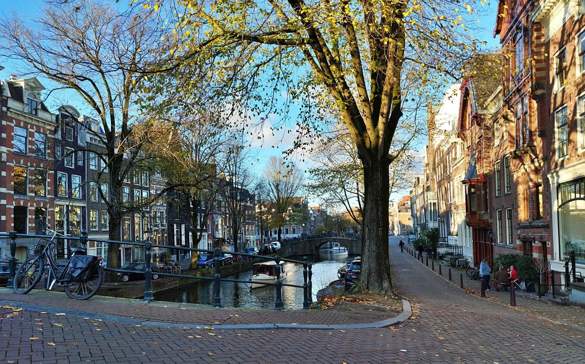 Eine Kanalstraße in Amsterdam mit geparkten Fahrrädern, klassischen niederländischen Häusern, einer Brücke und baumgesäumten Wegen, ideal für städtische Fahrradrouten.