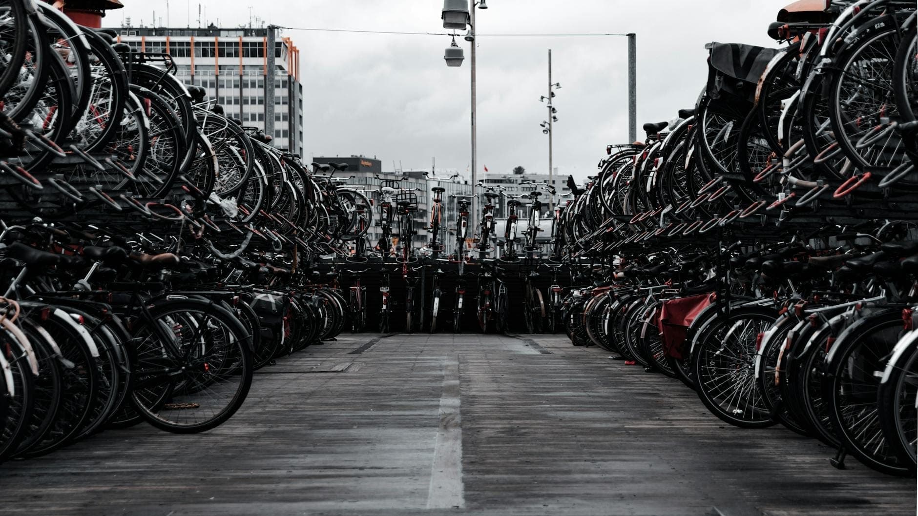 Reihen von Fahrrädern, die in einem mehrstöckigen Fahrradparkhaus in Amsterdam mit städtischen Gebäuden im Hintergrund geparkt sind.