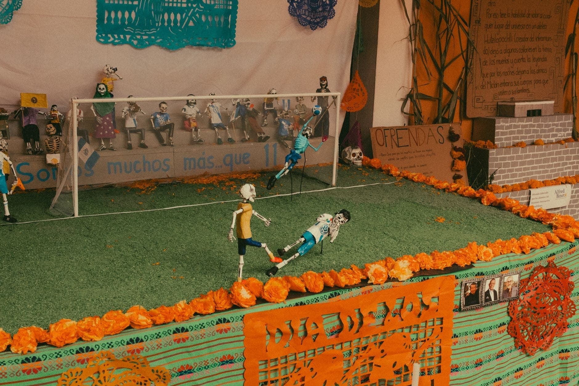 Un autel communautaire coloré du Día de los Muertos installé en plein air, décoré de soucis et de papiers découpés, avec des squelettes joueurs de football espiègle.