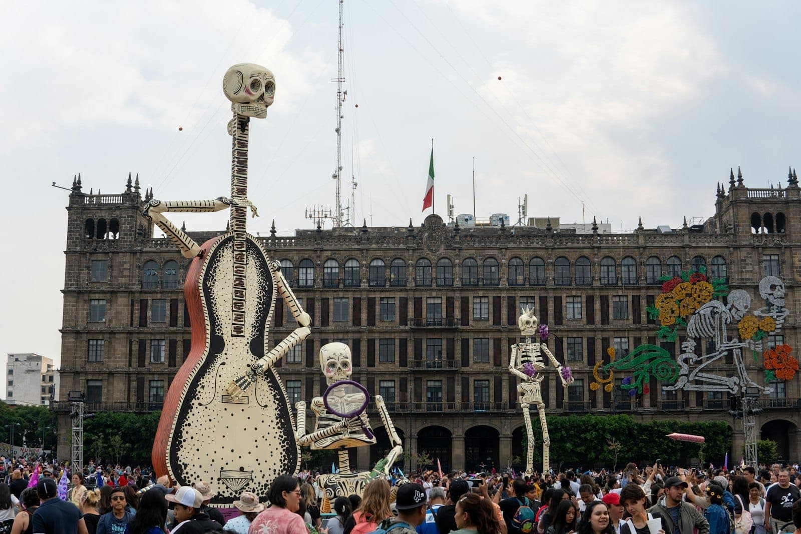 Le Zócalo bondé à Mexico City avec de gigantesques figurines de squelettes du Día de Muertos et des décorations devant un bâtiment historique.