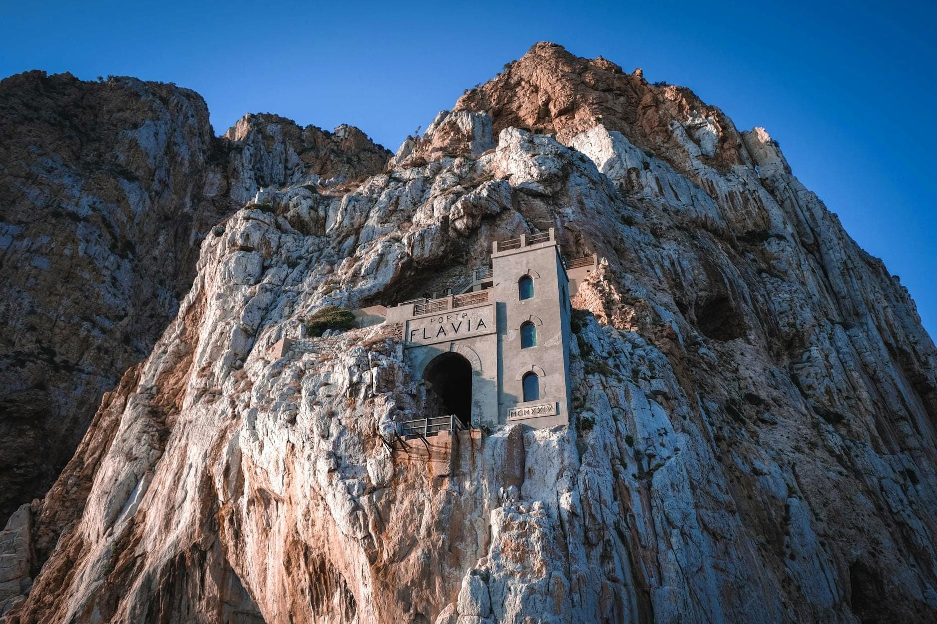 Estructura minera histórica construida en los dramáticos acantilados costeros, con la entrada al túnel de Porto Flavia en Cerdeña iluminada por la luz del sol.