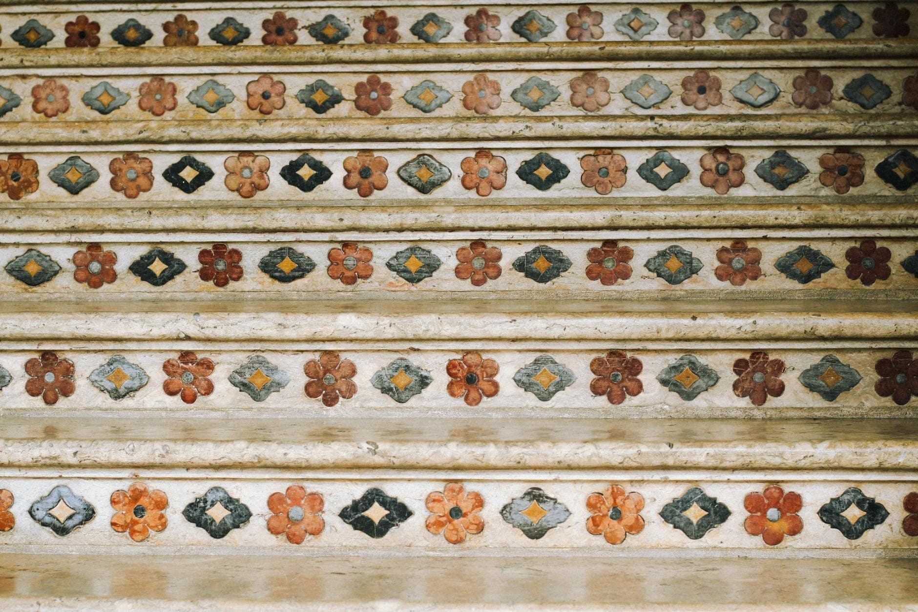 Foto close-up anak tangga berlapis keramik yang dihiasi motif bunga berwarna-warni, mengingatkan pada tangga terkenal di Caltagirone, Sisilia.