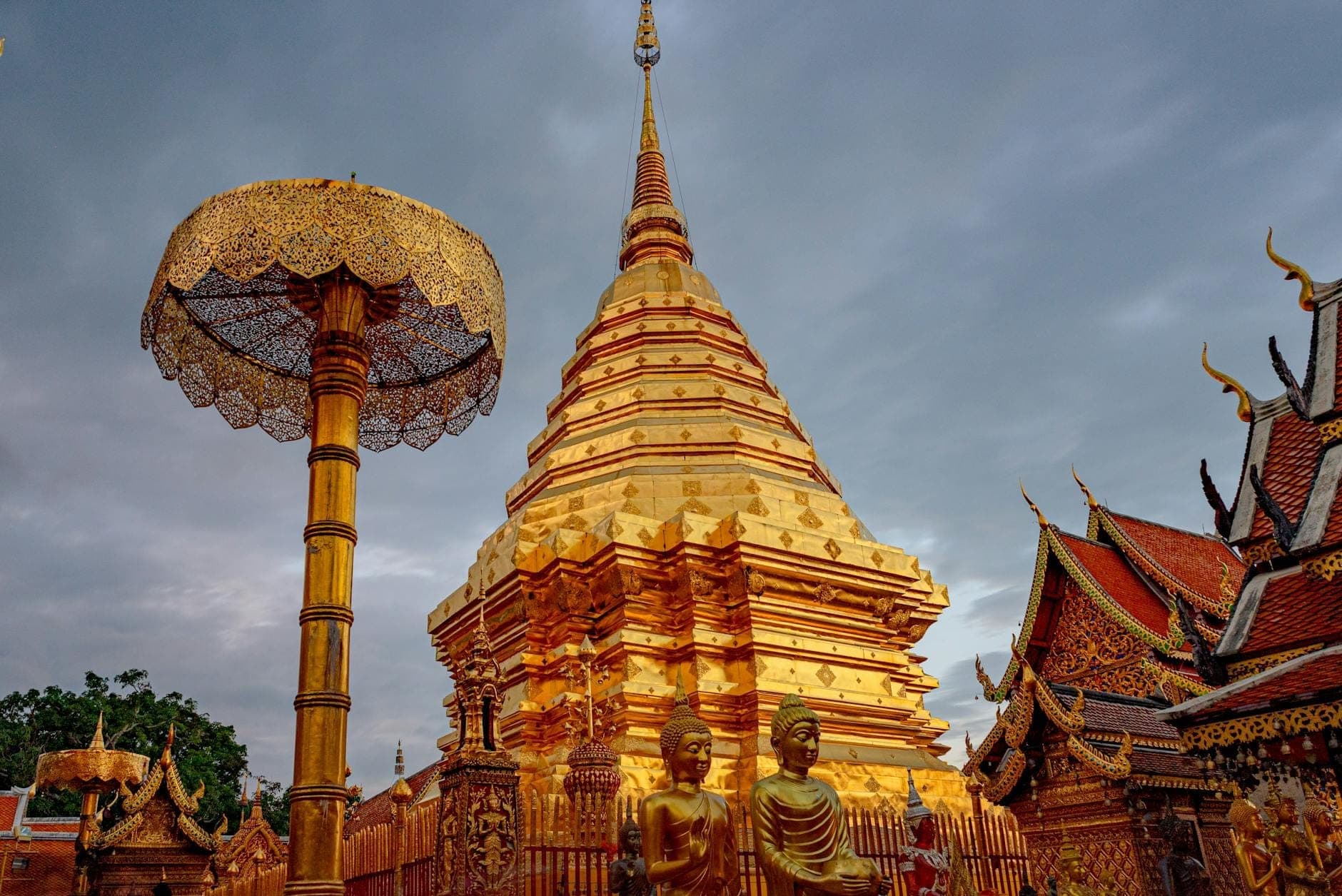 Chedi dorato e strutture ornate di Wat Phra That Doi Suthep a Chiang Mai sotto un cielo nuvoloso.