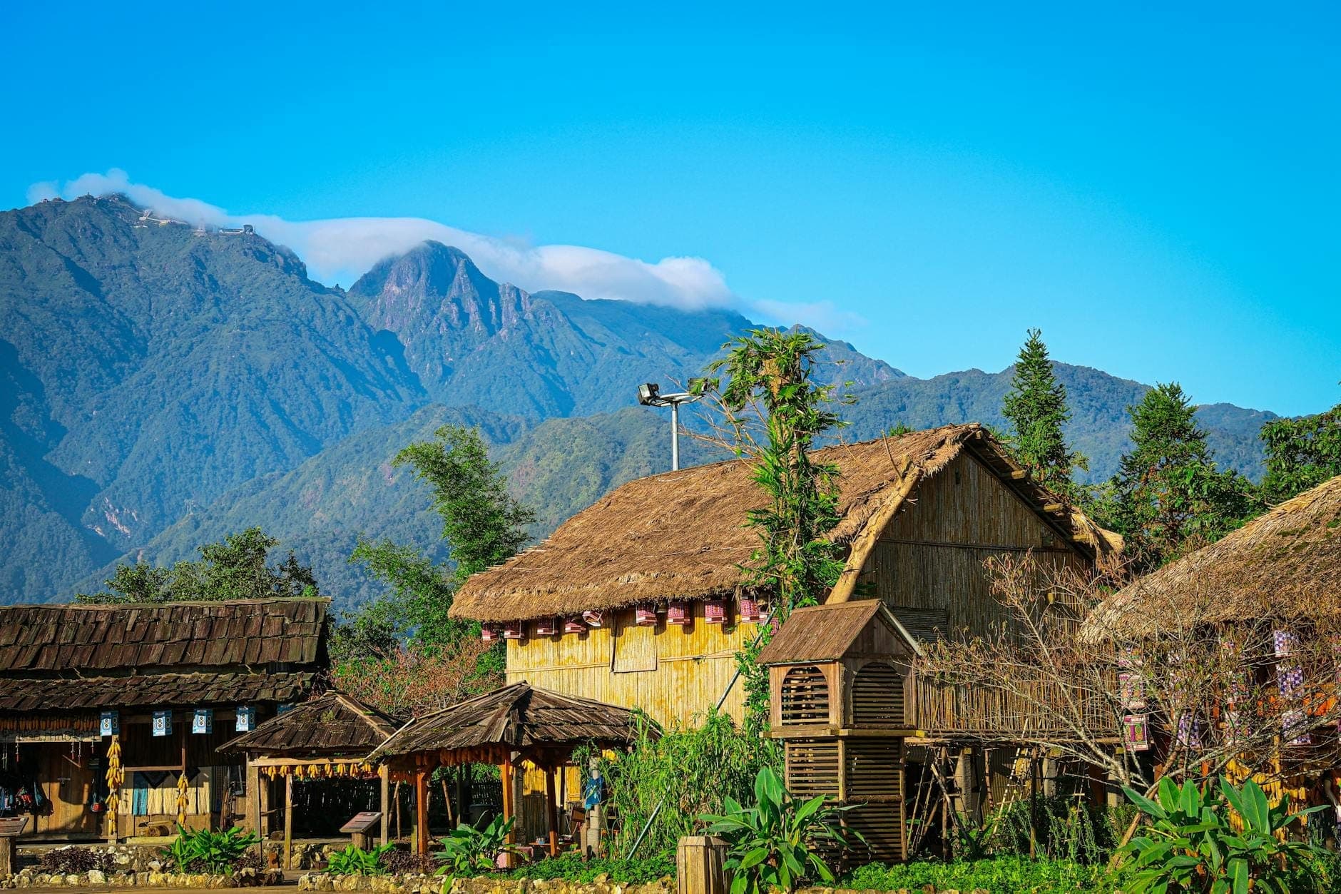 Edifici tradizionali in legno e con tetto di paglia davanti a spettacolari montagne calcaree vicino a Chiang Dao, nel nord della Thailandia, sotto un cielo azzurro limpido.