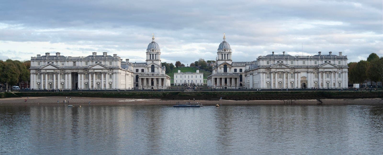 Panoramablick auf das Old Royal Naval College von der gegenüberliegenden Themseseite unter bewölktem Himmel, UNESCO-Weltkulturerbe in Greenwich, London.