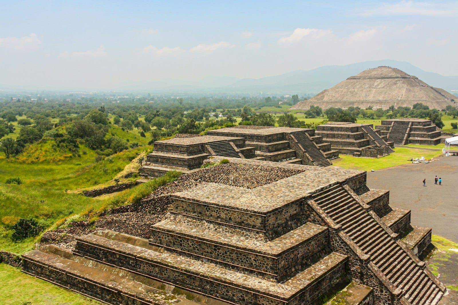 Pirámides de piedra en el sitio arqueológico de Teotihuacán con la Pirámide del Sol al fondo y exuberante vegetación verde.