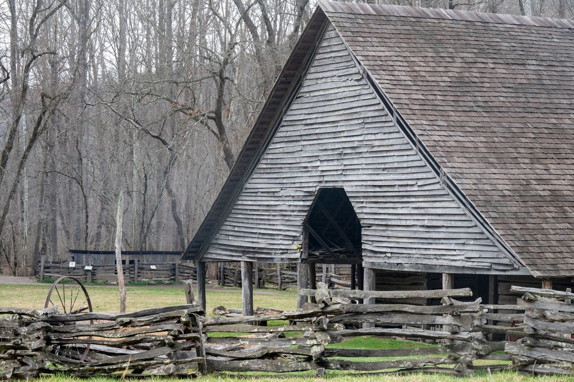 Storico fienile in legno con recinzione a binari spezzati davanti e alberi spogli sullo sfondo, che evoca un ambiente rurale del Tennessee del XIX secolo.