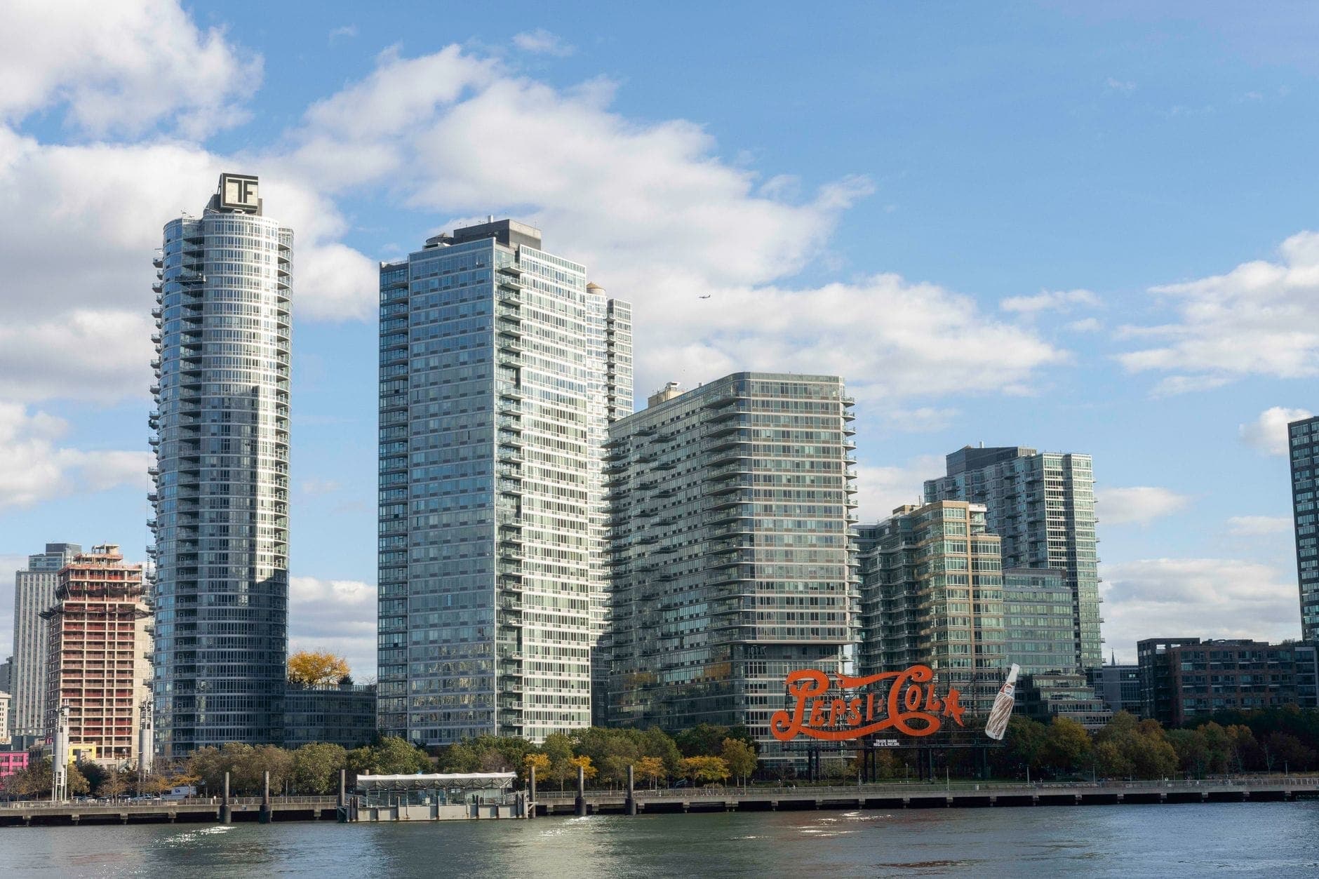 ริมน้ำของ Long Island City ในควีนส์ที่มีอาคารสูงสมัยใหม่และป้าย Pepsi-Cola อันเป็นสัญลักษณ์ มองเห็นจากฝั่งตรงข้ามของ East River ในวันที่แดดสดใส