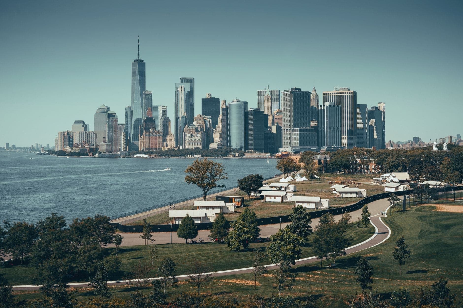 วิวกว้างของ Governors Island ในเบื้องหน้าพร้อมเส้นขอบฟ้าของ Lower Manhattan อีกฝั่งของท่าเรือในเบื้องหลังในวันที่อากาศแจ่มใส