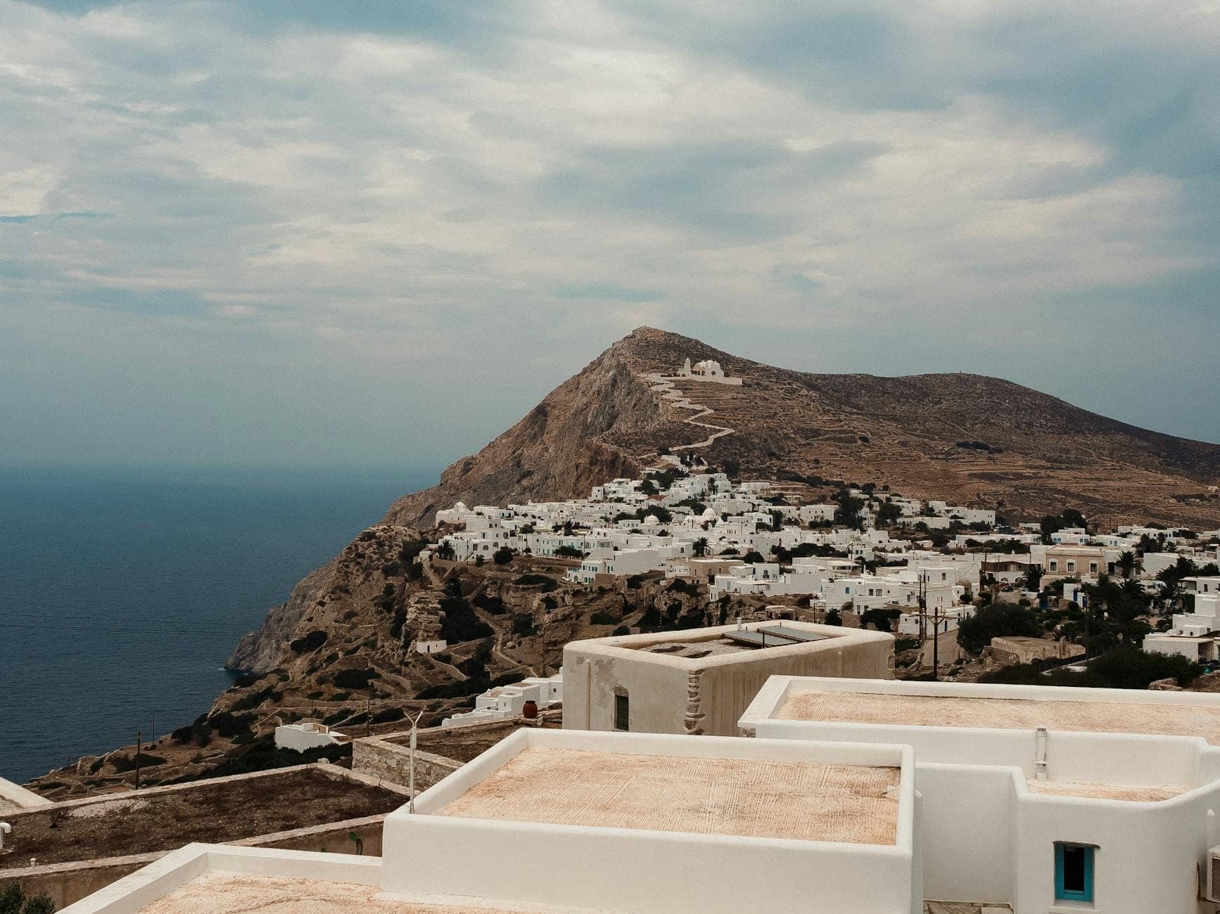 Vista panorámica de una isla de las Cícladas con edificios encalados en una colina con vistas al mar, típica de Ios o Folegandros cerca de Santorini.