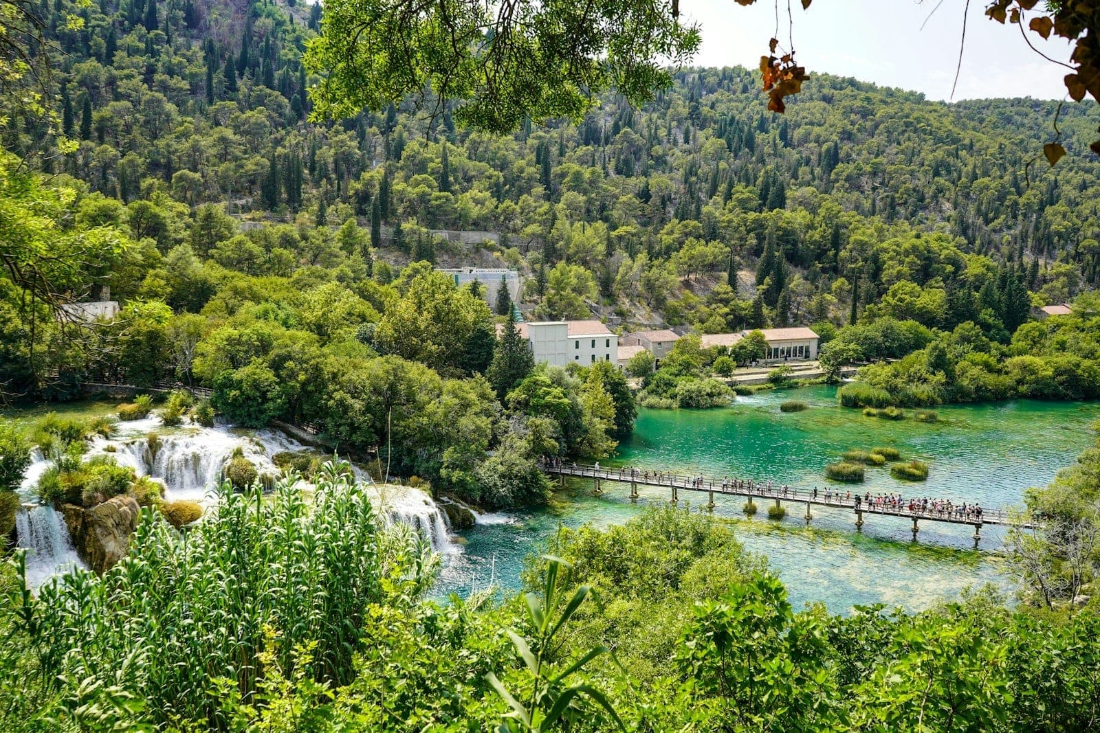 Vue panoramique des cascades de Skradinski buk, bassins turquoise, passerelle piétonne et végétation luxuriante par une journée ensoleillée.