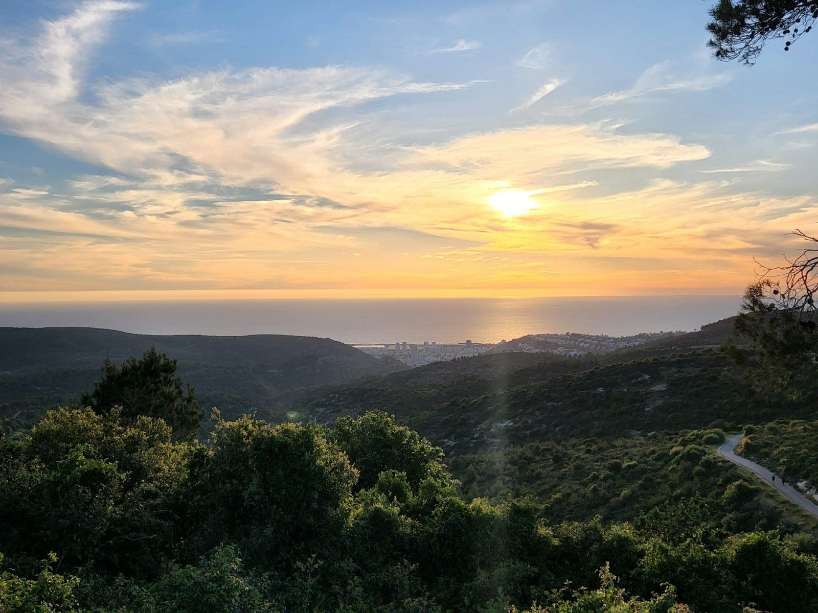 Vista panoramica su colline rigogliose e costa al tramonto con un sentiero tortuoso e la città in lontananza, Spalato, Croazia