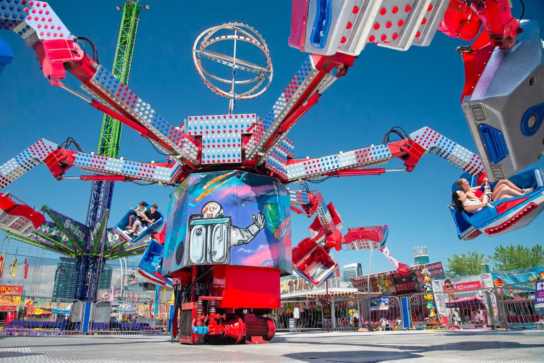 Atracción de parque de amusement brillante y colorida con personas sentadas en coches giratorios en una feria al aire libre en un día soleado.