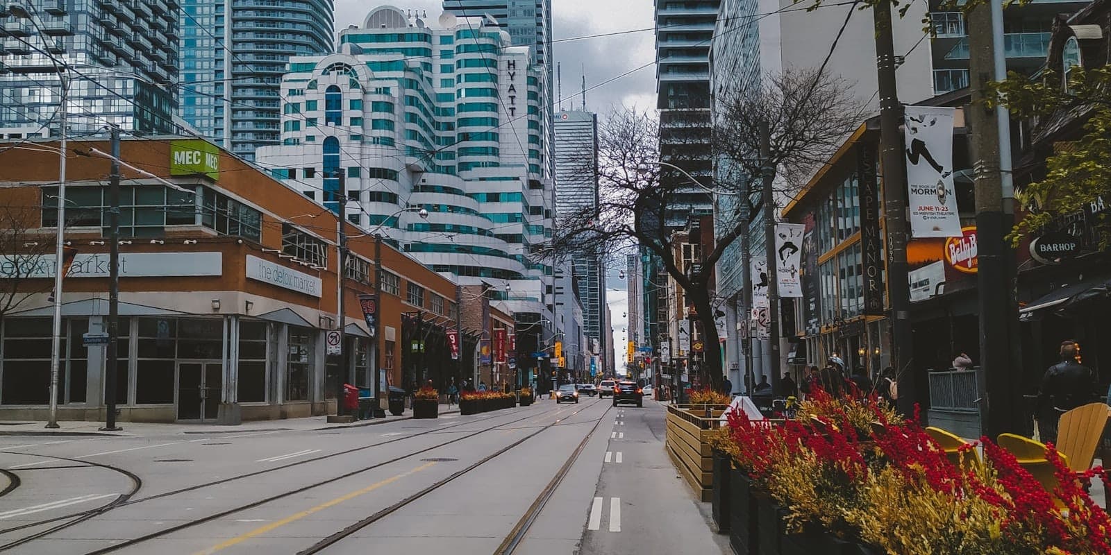 Vista de una concurrida calle del centro de Toronto con edificios modernos, tiendas minoristas y vías de tranvía en un día nublado.