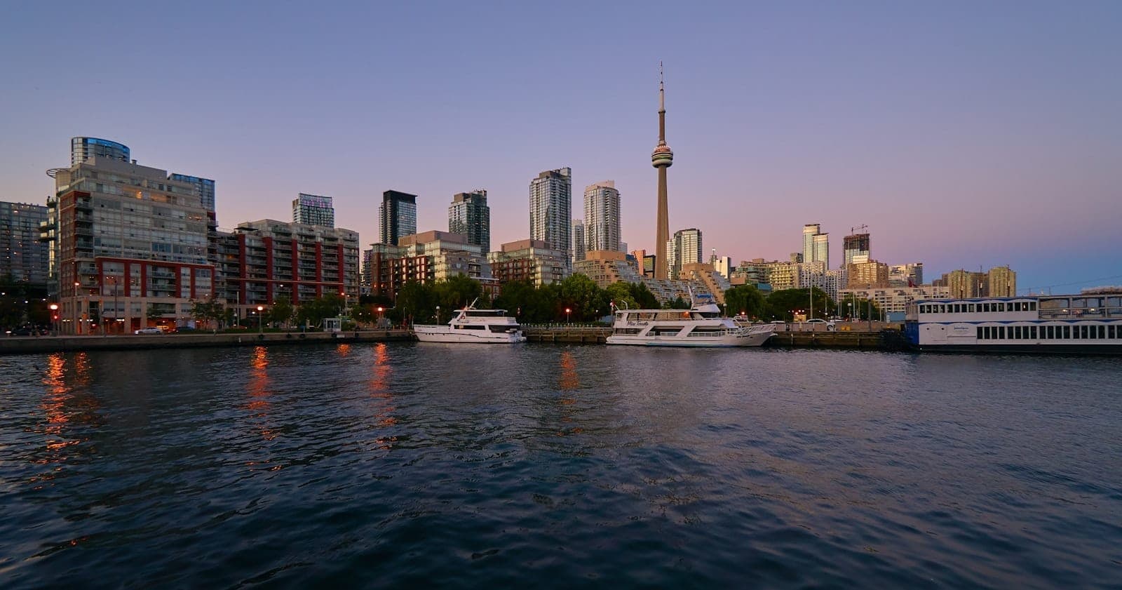Puerto de Toronto con barcos atracados a lo largo del puerto, horizonte moderno y la CN Tower al fondo al atardecer.