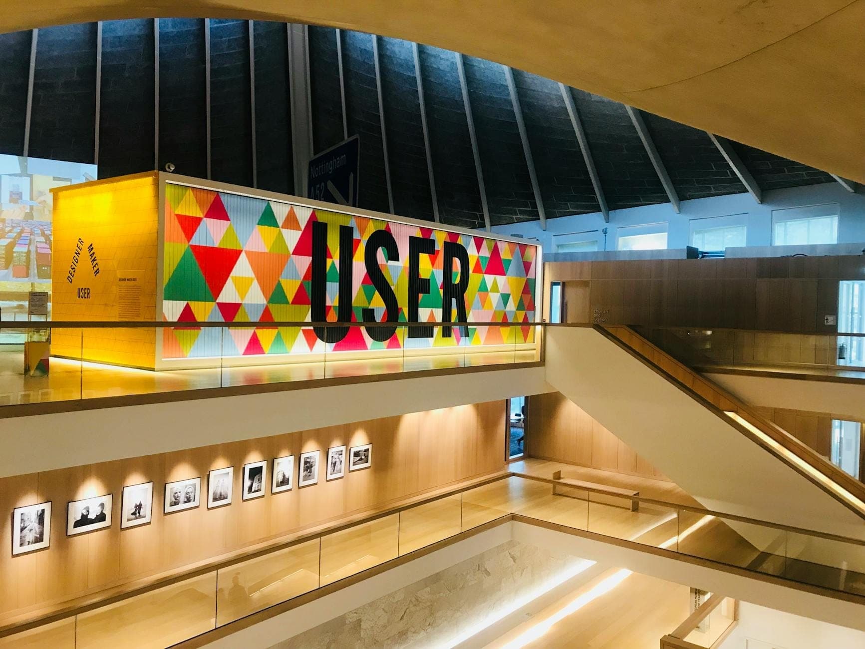 Interior of the Design Museum in London with modern angular architecture, bright lighting, a colorful geometric wall, and framed black and white photographs on display.