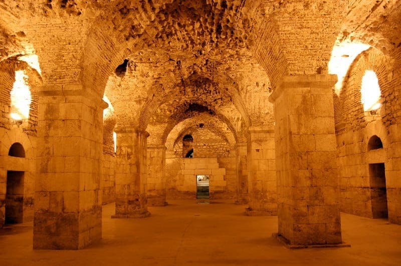 Archi e colonne in pietra all'interno delle Cantine di Diocleziano a Split, illuminate da luci calde, che mostrano l'antica architettura romana.