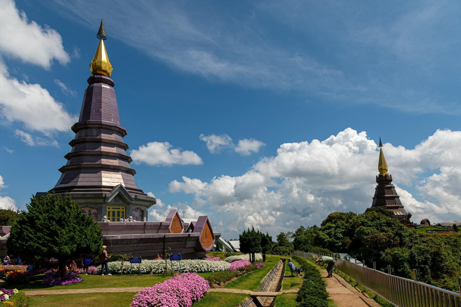 Zwei Königliche Zwillingstempel mit goldenen Turmspitzen, umgeben von bunten gepflegten Gärten unter einem strahlend blauen Himmel mit flauschigen Wolken auf dem Doi Inthanon.