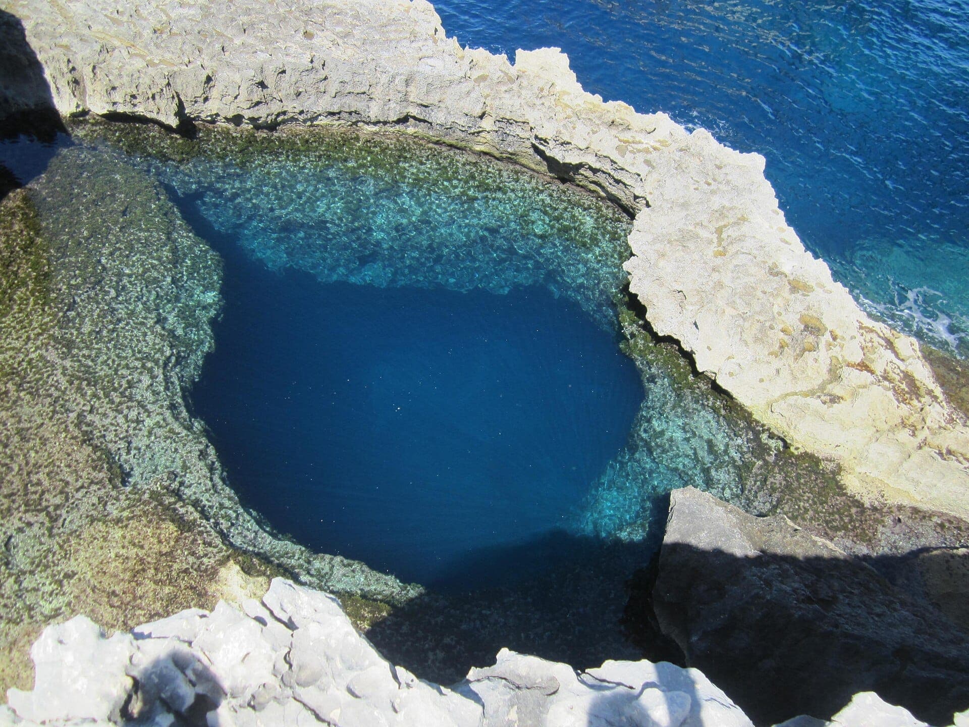 Luftaufnahme des Blue Hole bei Dwejra, Gozo, mit klarem blauem Wasser, umgeben von zerklüfteten Kalksteinformationen.