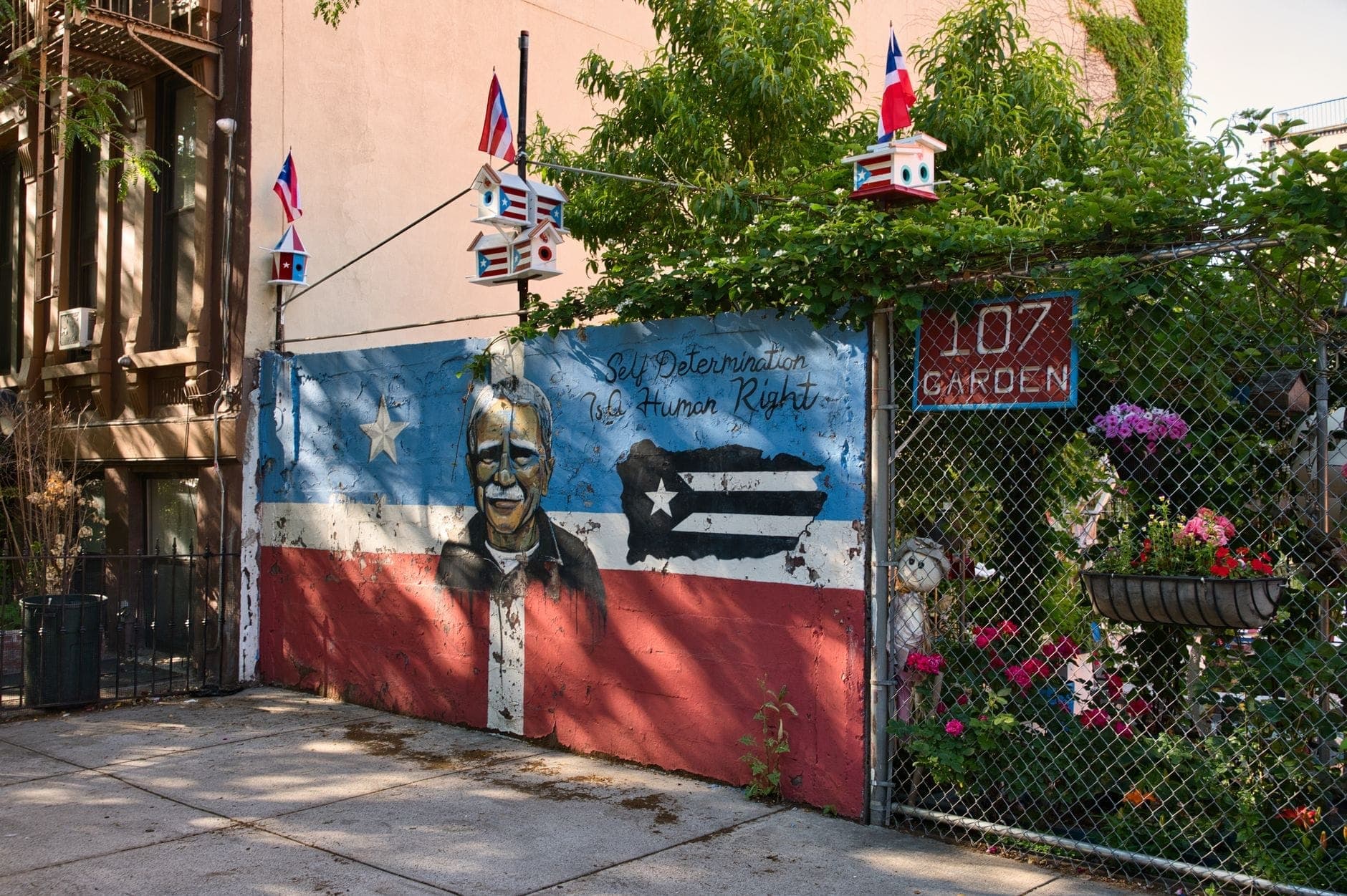 ภาพจิตรกรรมฝาผนังสีสดใส มีธงเปอร์โตริกันในสวนชุมชน East Harlem ตกแต่งด้วยธงเล็กและดอกไม้ วันแดดจ้า