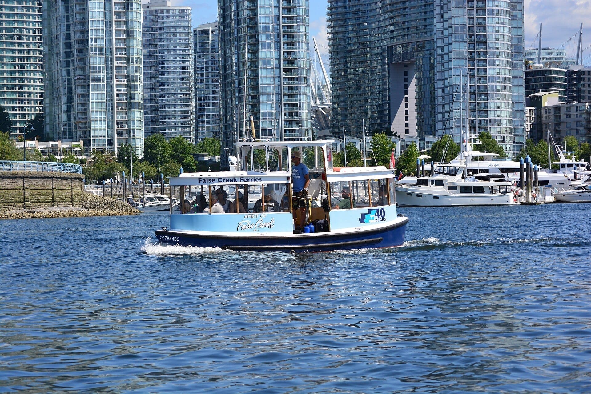 เรือสีน้ำเงินของ False Creek Ferries พาผู้โดยสารข้ามทางน้ำของ Vancouver โดยมีตึกสูงสมัยใหม่และเรือยอชต์เป็นฉากหลัง