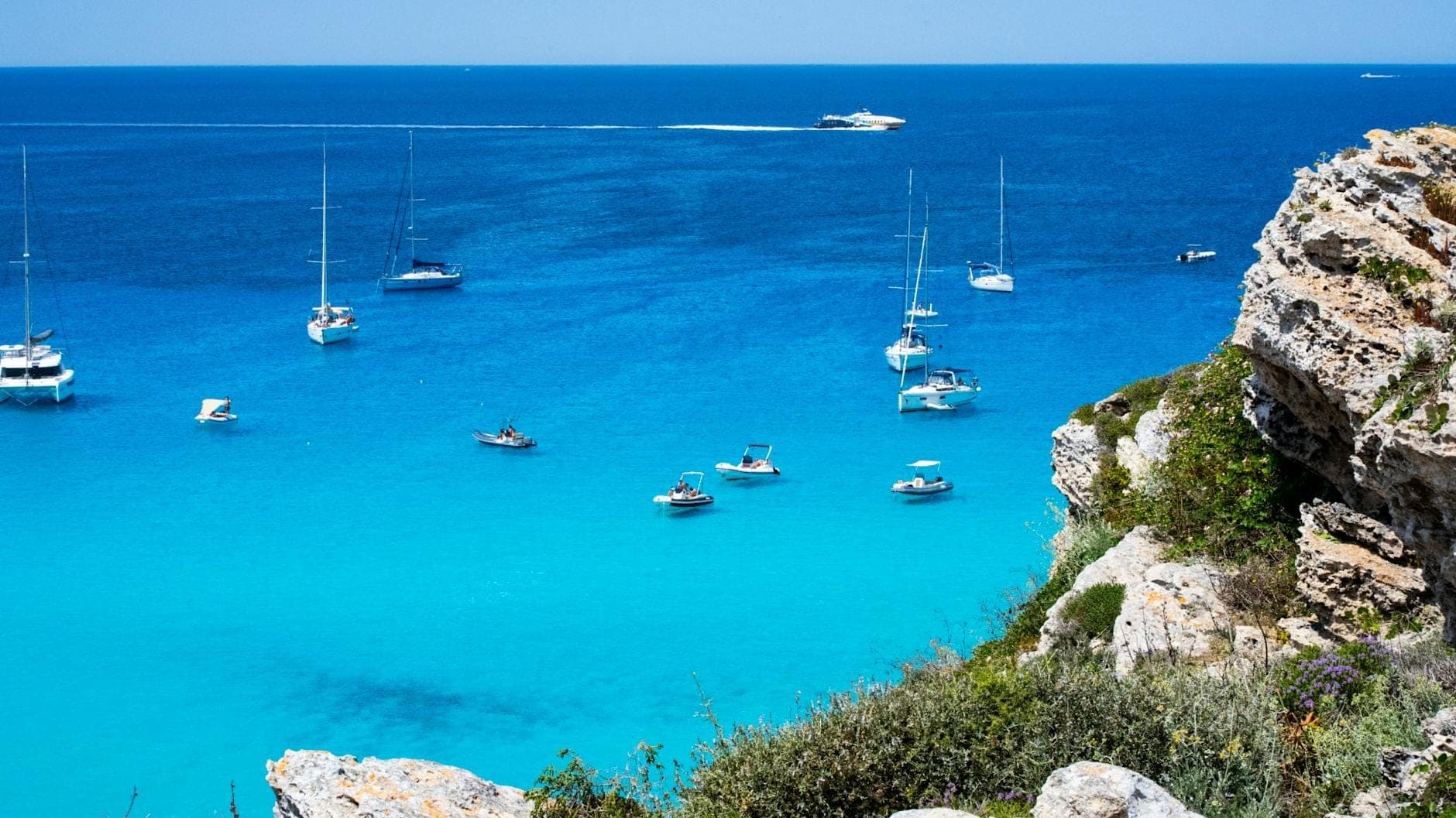 Pemandangan menakjubkan laut biru kehijauan Favignana dengan beberapa perahu layar dan tebing berbatu, memperlihatkan pesona pesisir pulau yang begitu mengundang di tengah keindahan Mediterania.