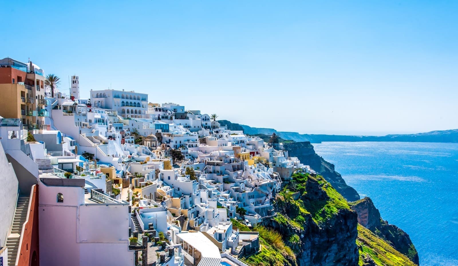 Panoramablick auf Fira mit weiß getünchten Häusern auf Klippen über dem tiefblauen Ägäischen Meer unter strahlend blauem Himmel.