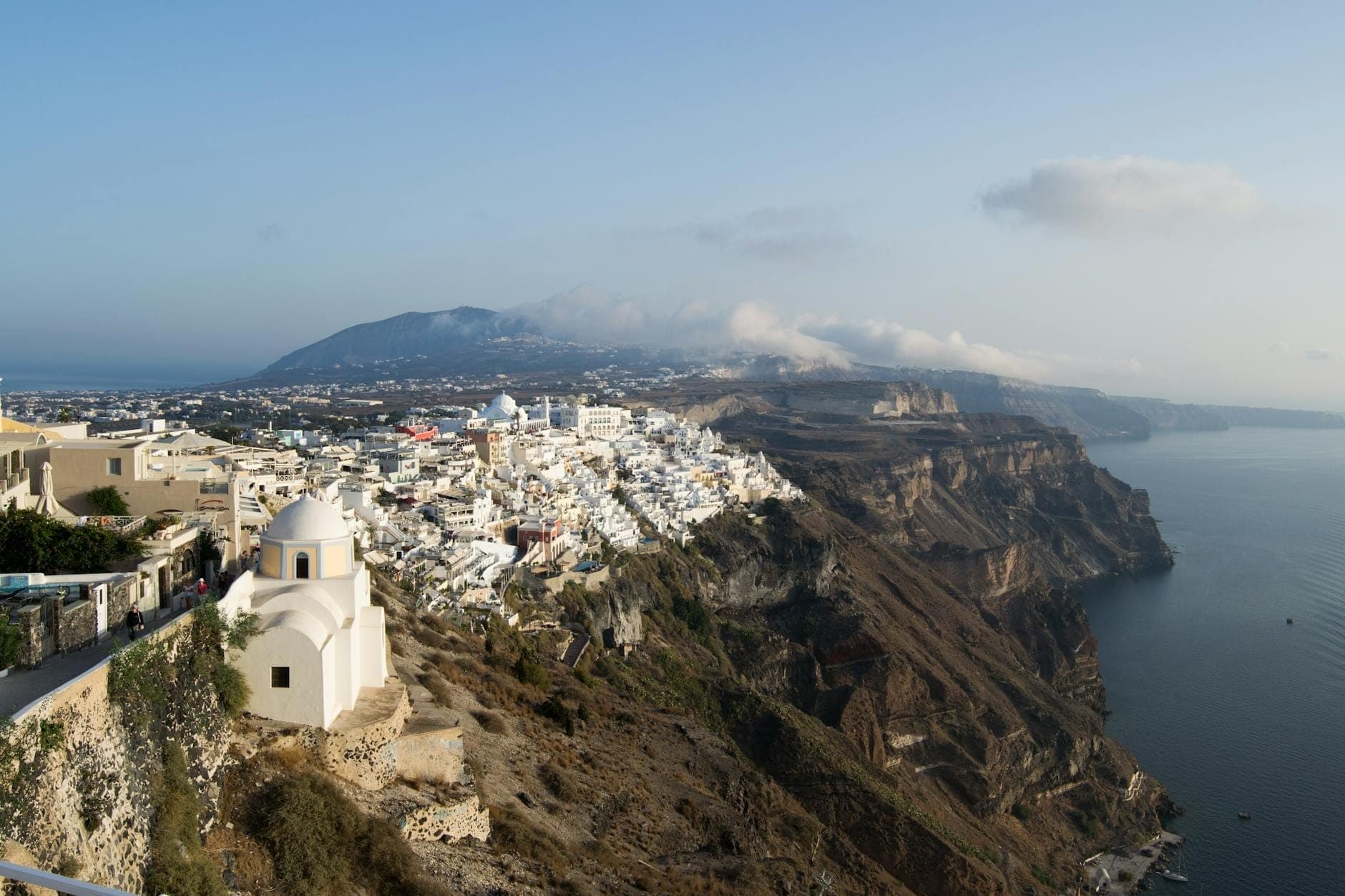Panoramablick auf das Dorf Firostefani mit weißgekalkten Häusern am Caldera-Rand Santorins, mit Blick auf dramatische Klippen und das blaue Ägäische Meer.