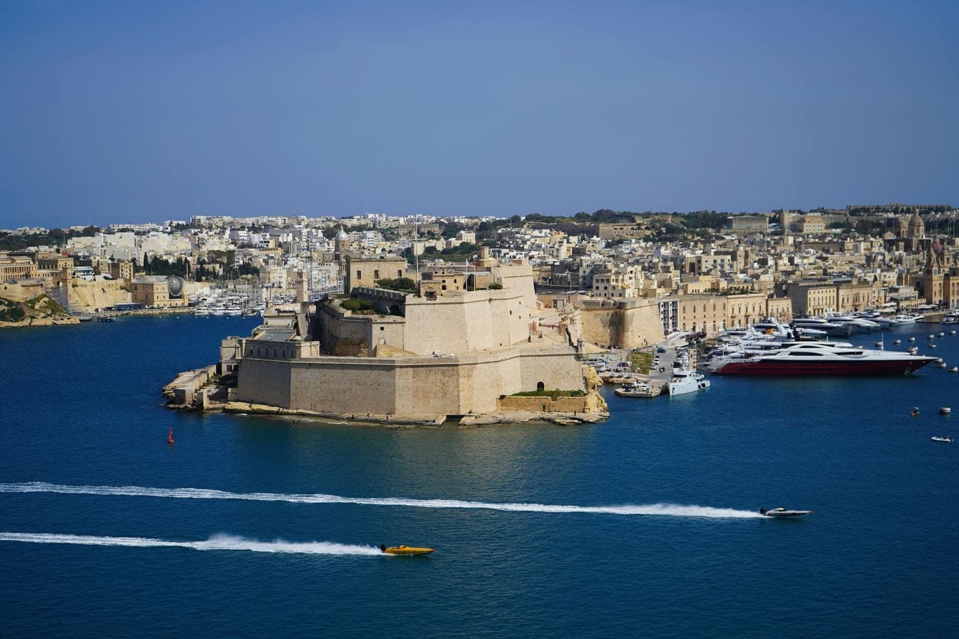 Panoramablick auf Fort St. Angelo, das in den Grand Harbour hineinragt, umgeben von tiefblauem Wasser, Booten und der Stadtkulisse von Birgu, Malta.