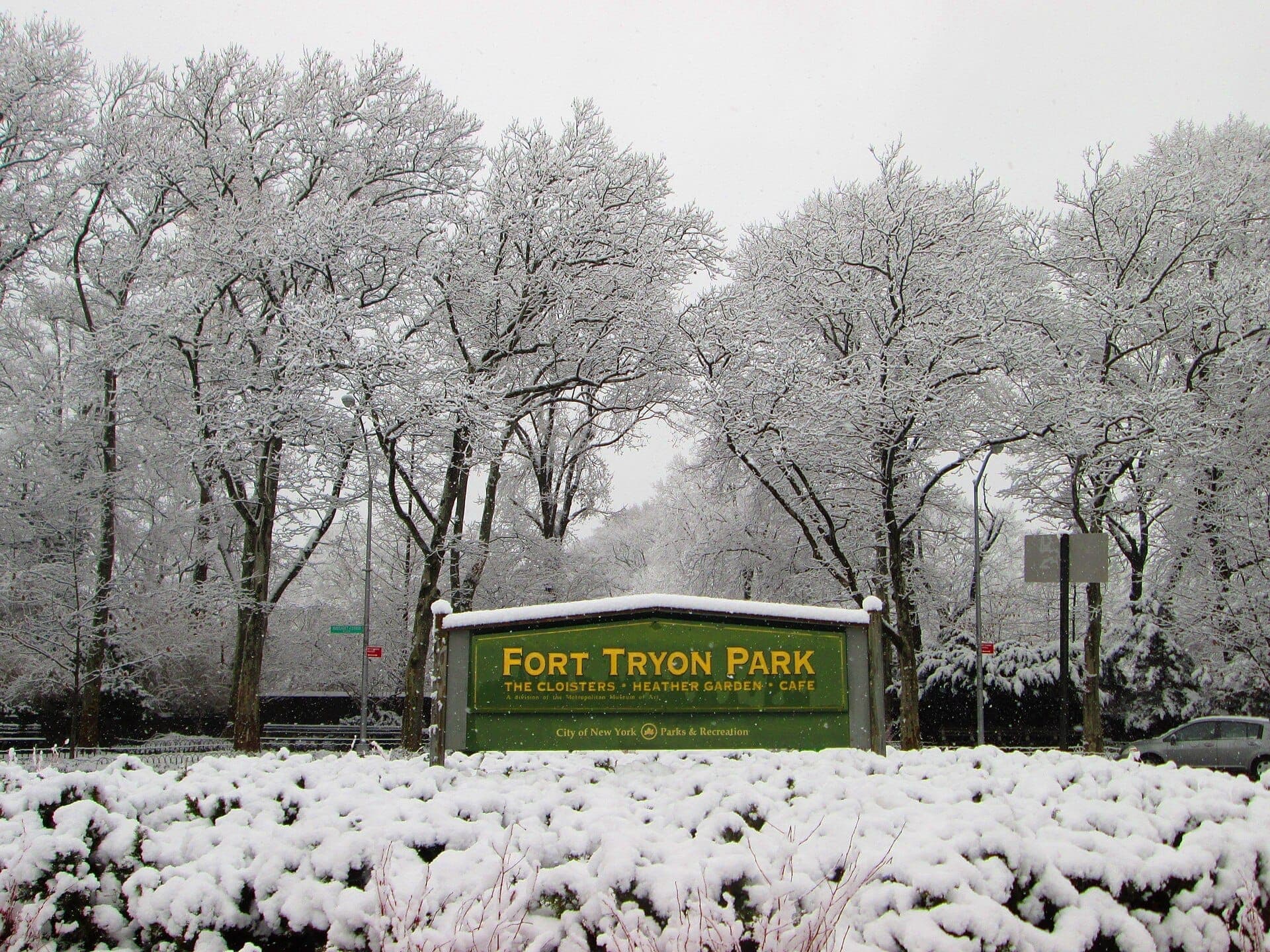 ป้ายทางเข้า Fort Tryon Park ล้อมรอบด้วยต้นไม้และพุ่มไม้ที่ปกคลุมด้วยหิมะในวันฤดูหนาวที่มีเมฆมากในแมนฮัตตัน