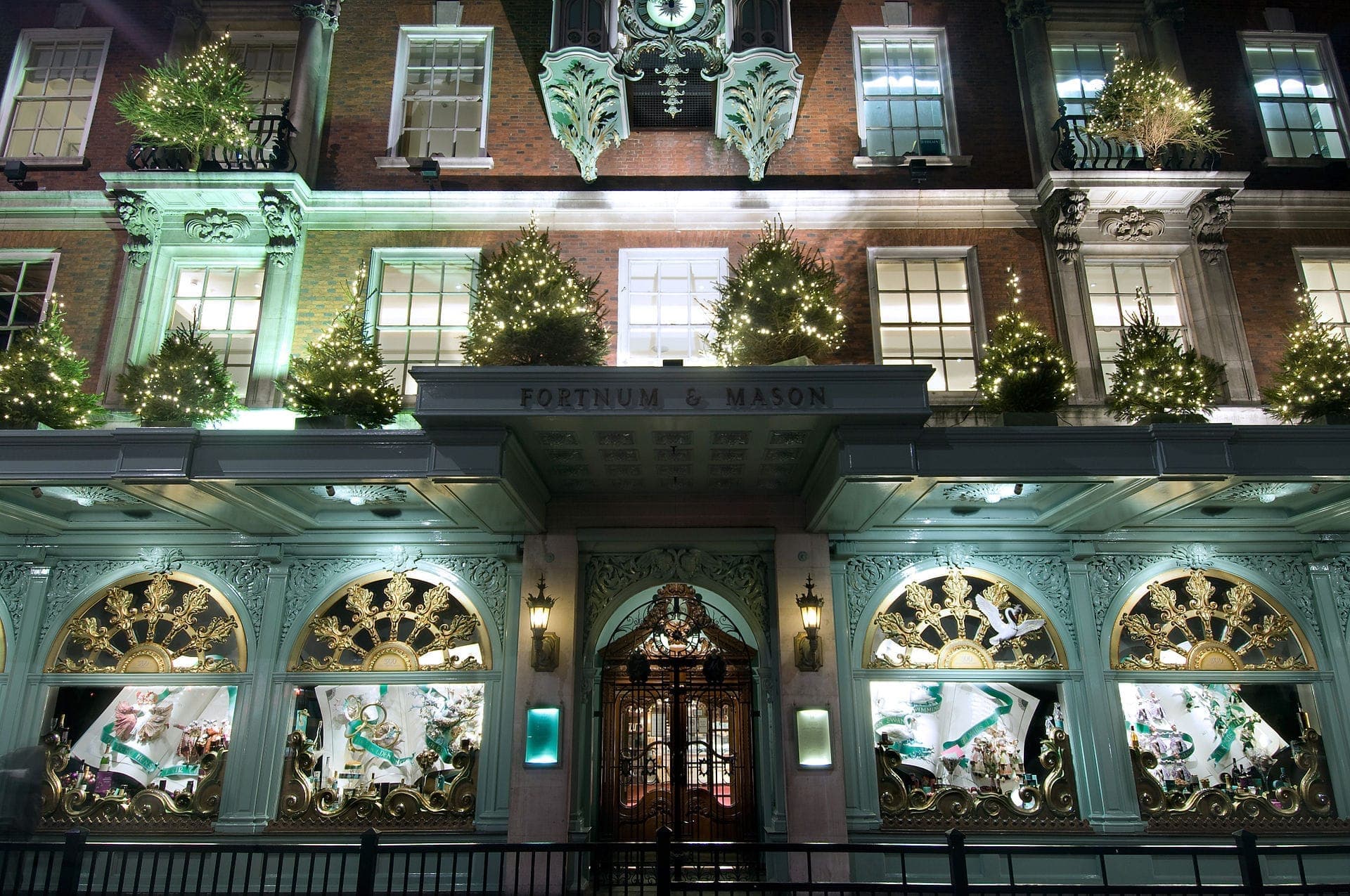 Die erleuchtete Fassade von Fortnum & Mason in London, geschmückt mit funkelnden Weihnachtsbäumen und kunstvollen Schaufenstern bei Nacht.