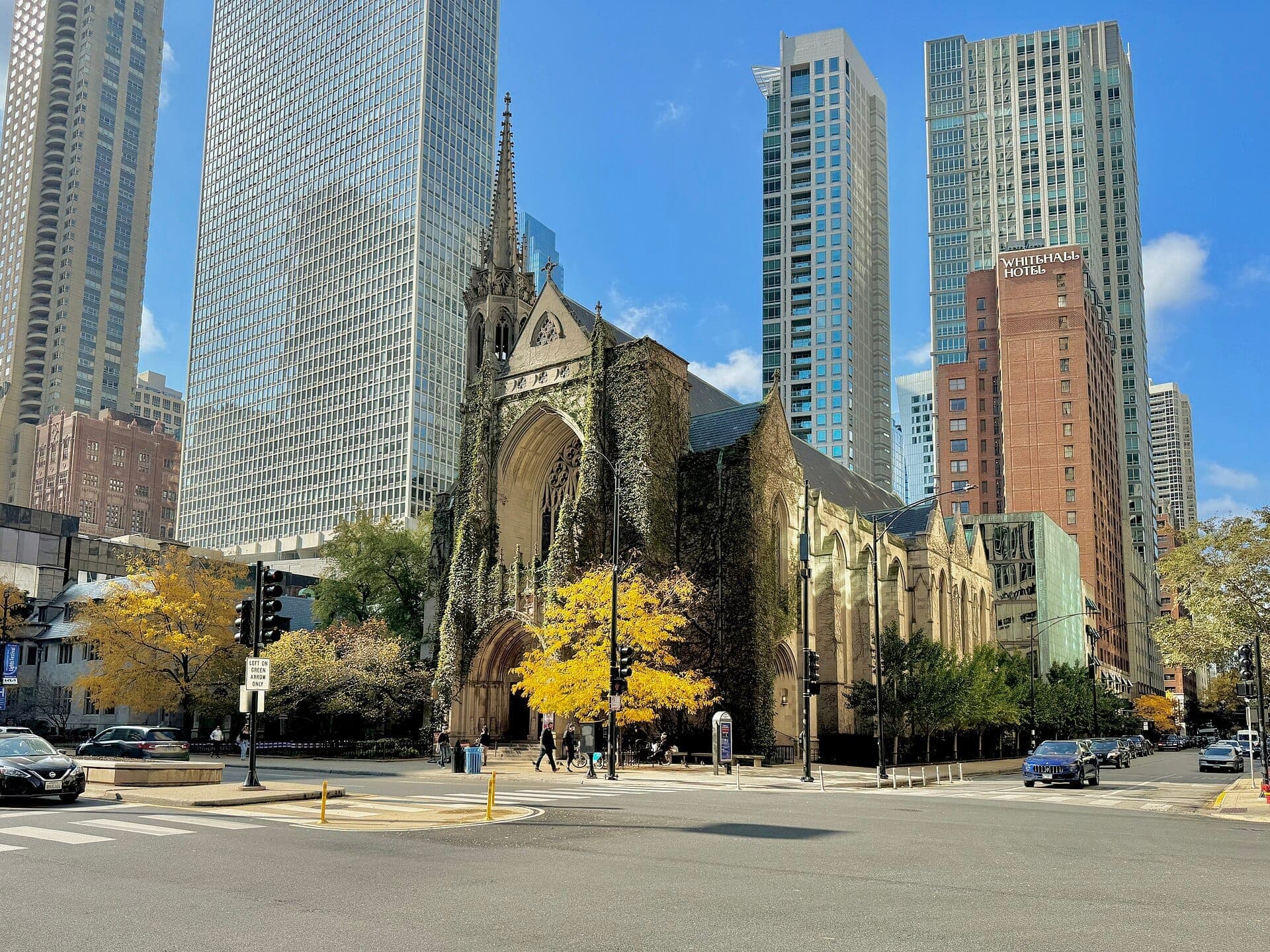 Fourth Presbyterian Church in Chicago framed by autumn trees, with Gothic architecture standing out against surrounding modern skyscrapers and blue sky.