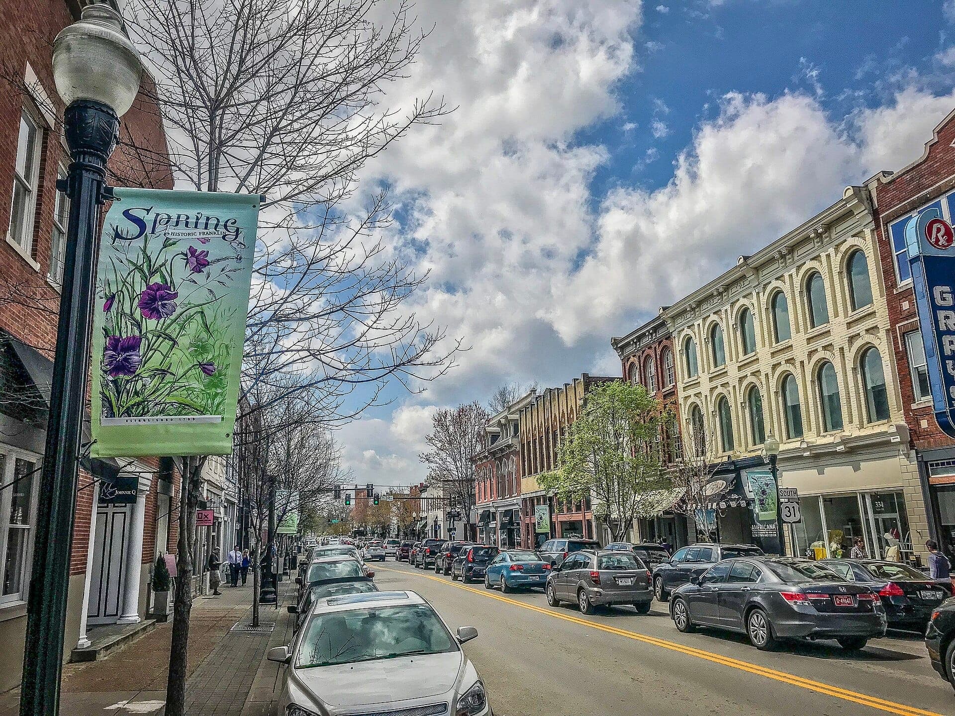Historic Main Street in Downtown Franklin with rows of 19th-century brick buildings, parked cars, and a spring floral banner on a sunny day.