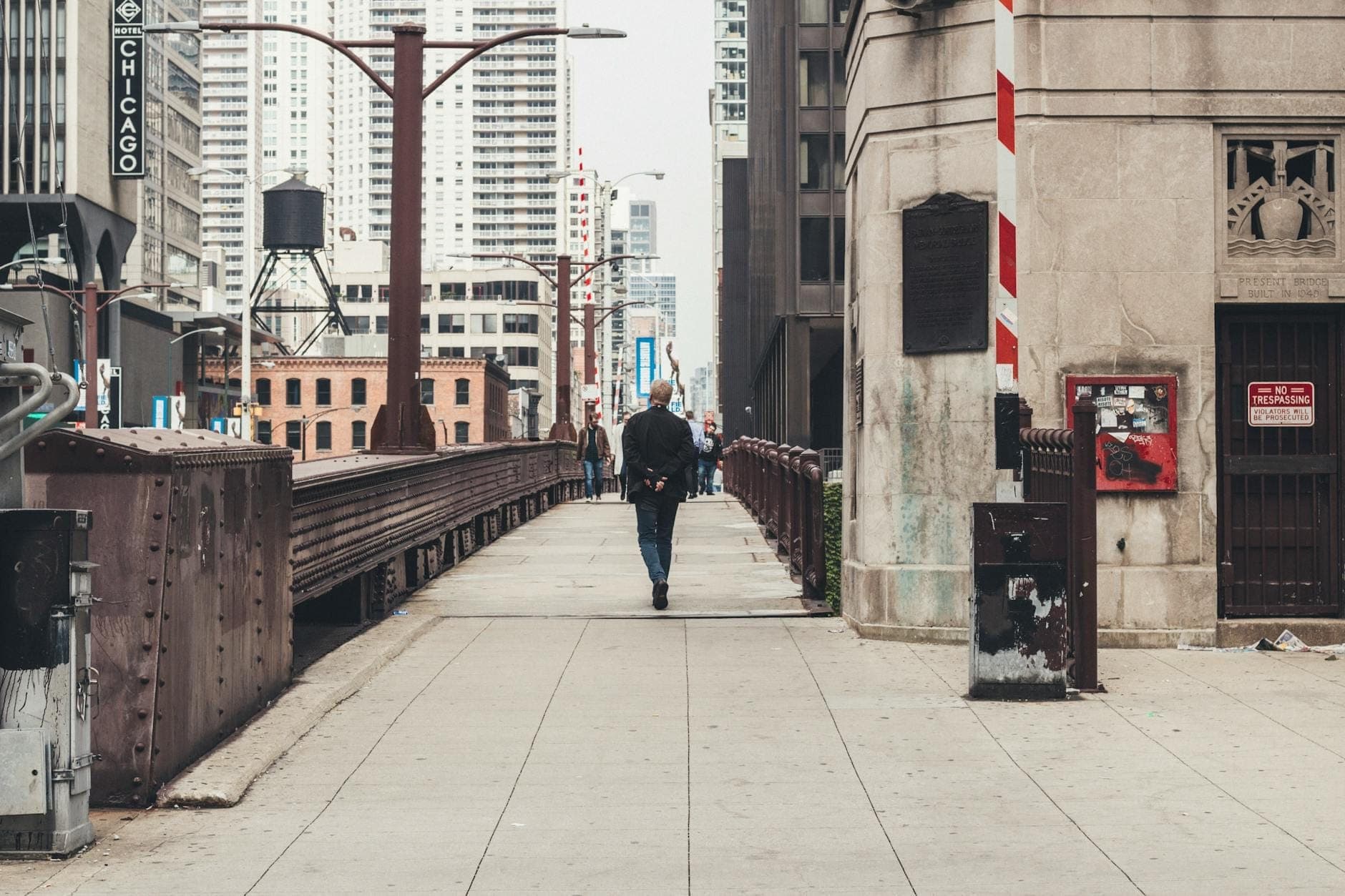 Person walking on a Chicago city bridge with skyscrapers and urban architecture in the background.