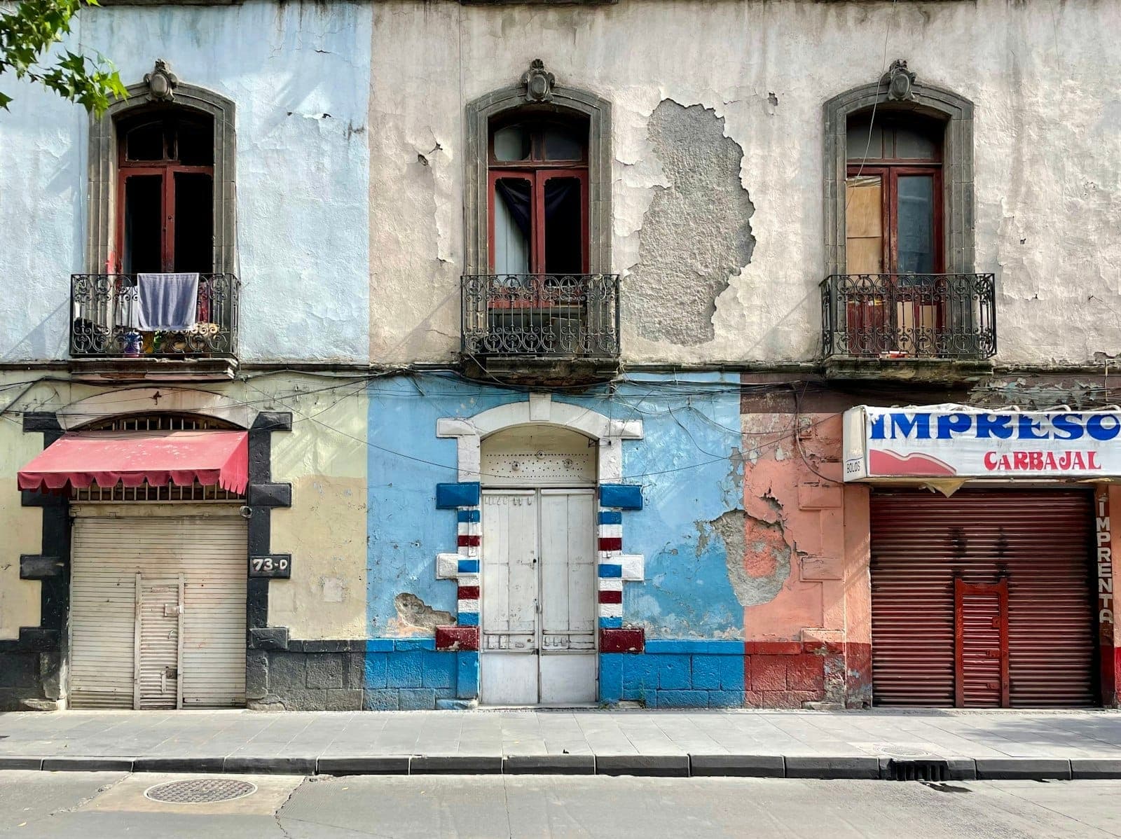 Colorful, weathered colonial building with balconies and closed shop fronts on a quiet street in Mexico City.
